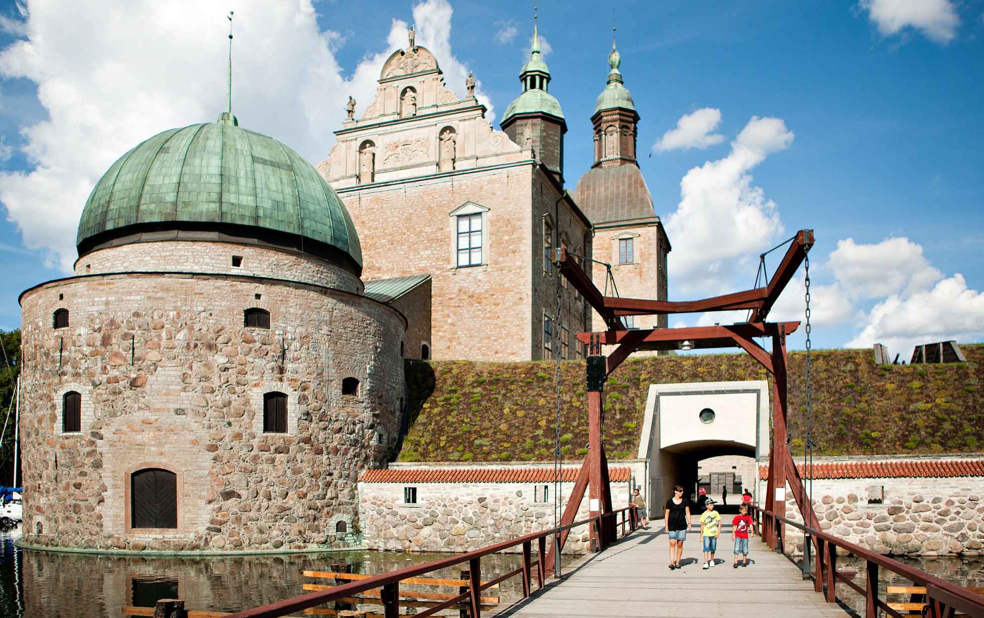 Trois enfants sont sur un pont menant au château de Vadstena, qui est entouré d'un mur, d'une haie et de douves.