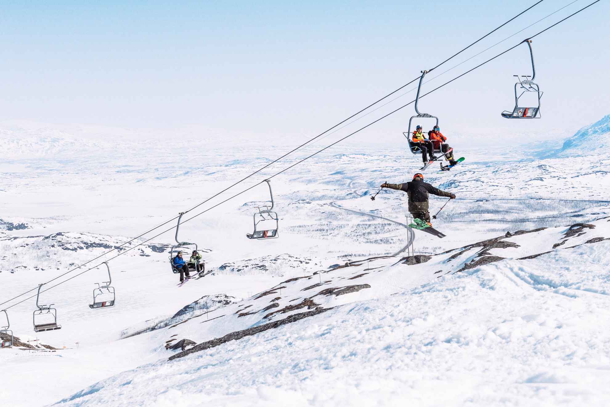 Des personnes sont assises sur un téléski et regardent une personne qui saute avec des skis.