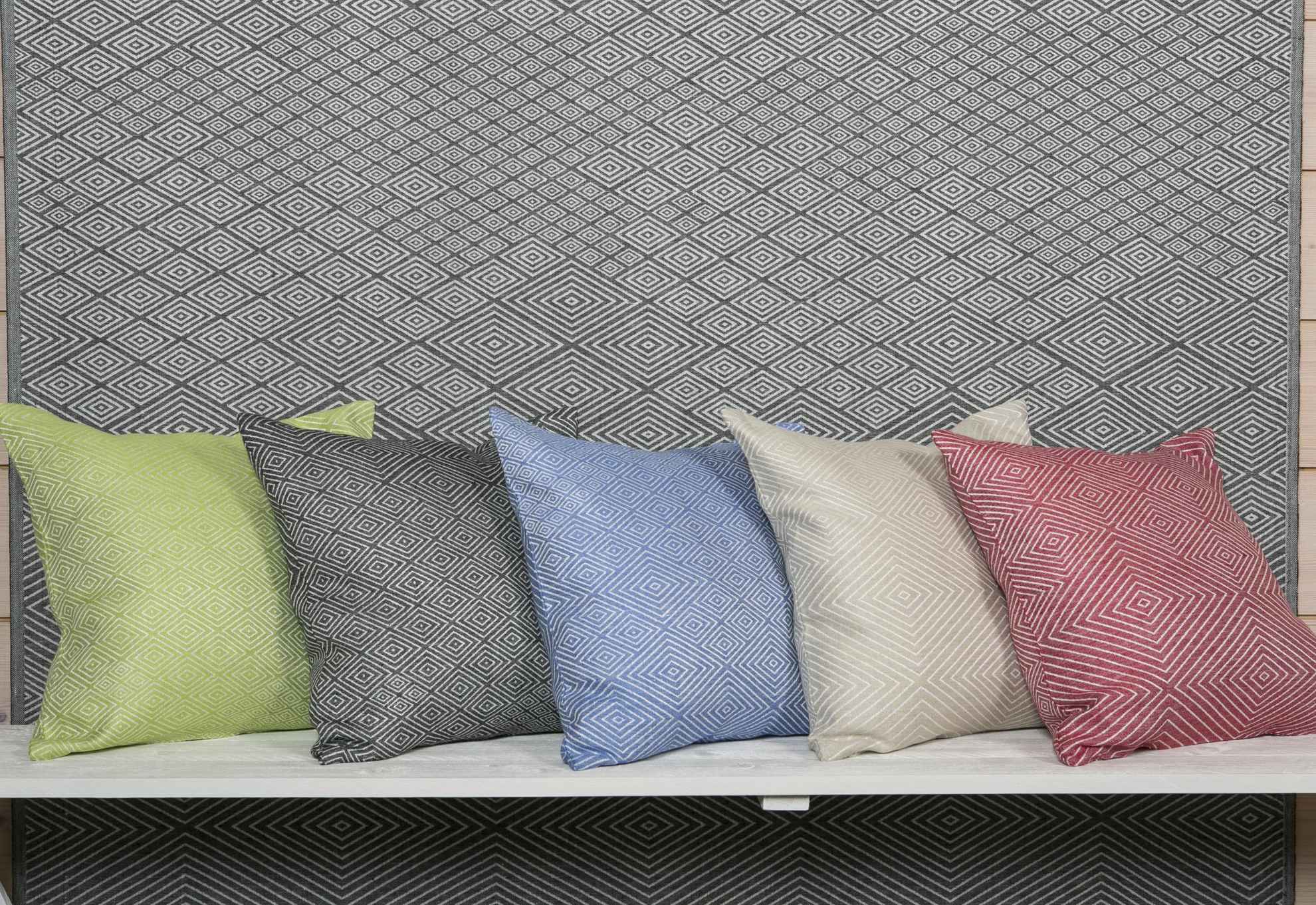 Cinq oreillers de couleurs différentes avec un motif symétrique sont posés devant un tissu gris avec le même motif.