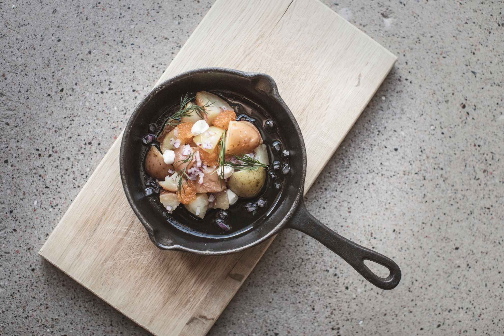 Gros plan sur un plat de caviar accompagné de pommes de terre et d'oignons rouges servi dans une poêle en fer.