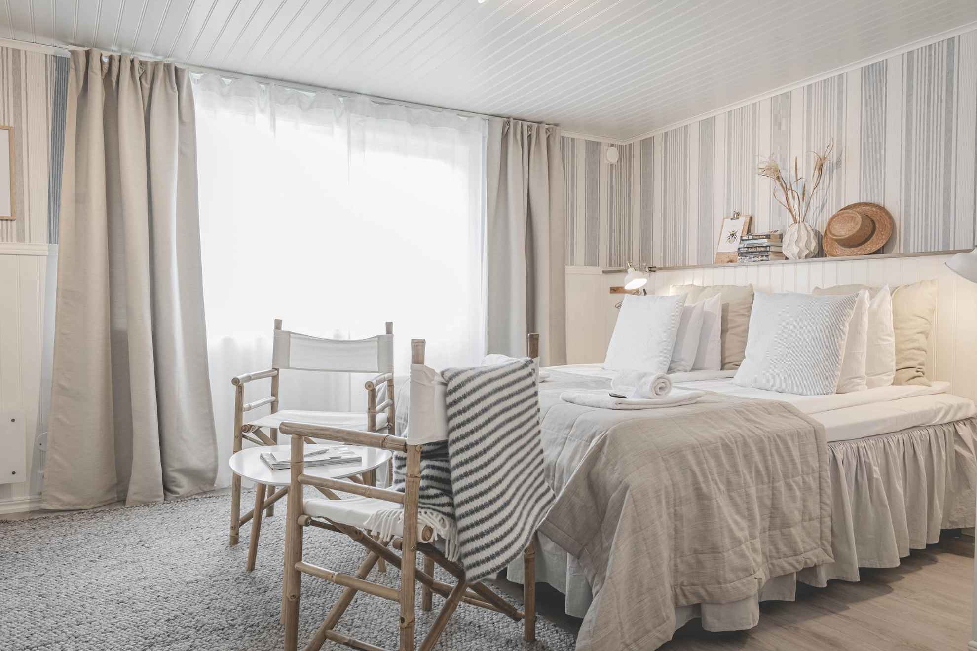 Une chaöbre d'hôtel de StrandNära. Le chambre dispose d'un grand lit et est décorée en blanc et beige.