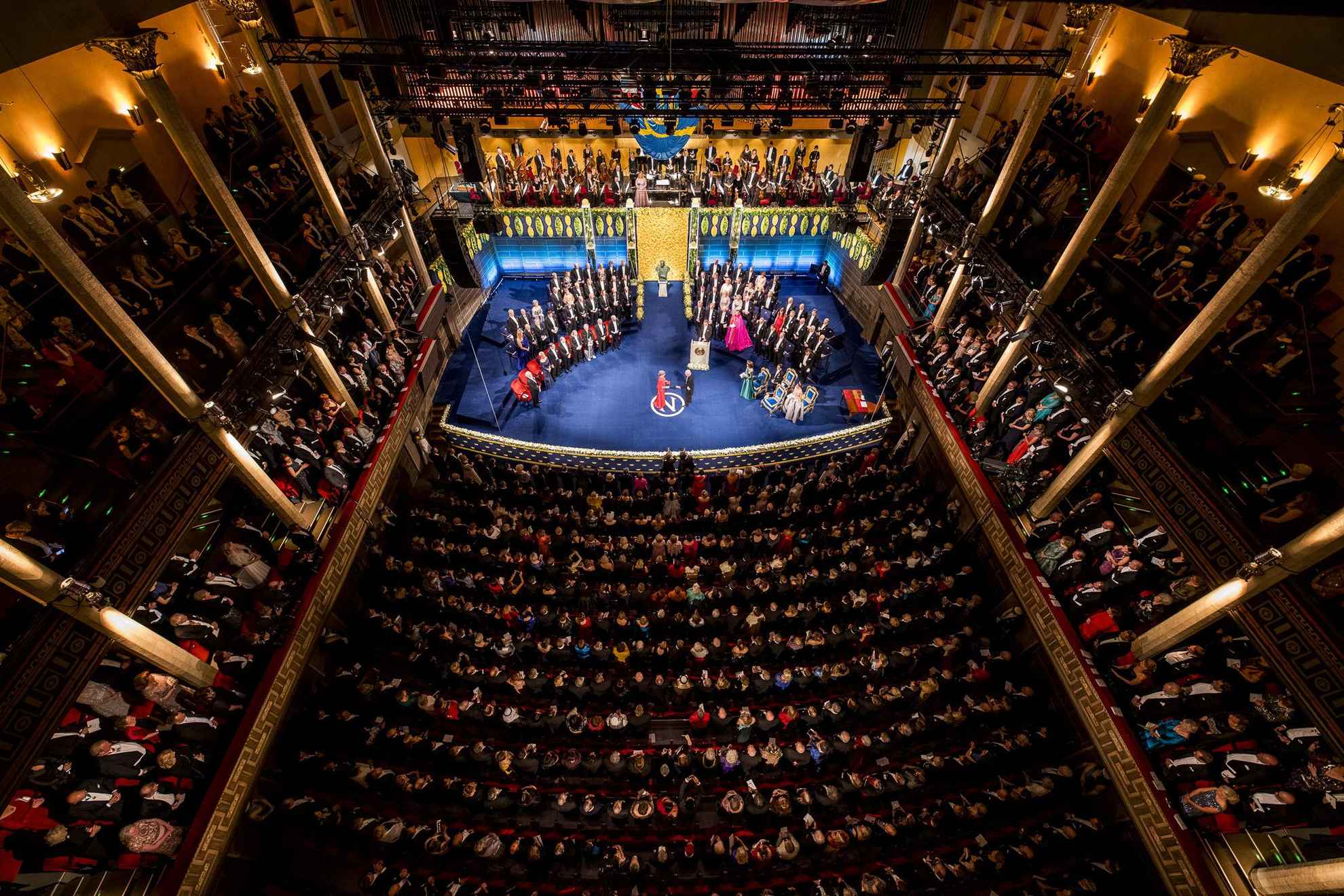 Une salle pleine de monde. Ils regardent la scène où les lauréats reçoivent leur prix Nobel.