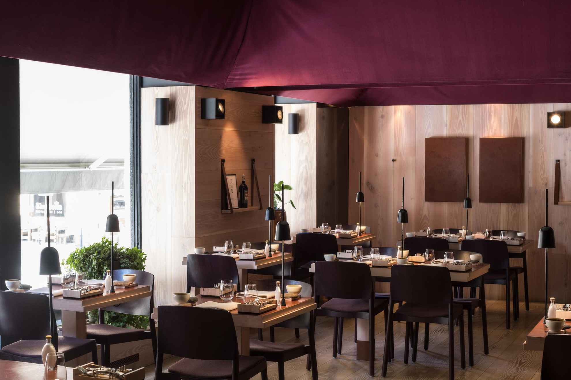 Vue sur l'intérieur d'un restaurant avec des tables dressées, des mur en bois clair et un plafond violet.
