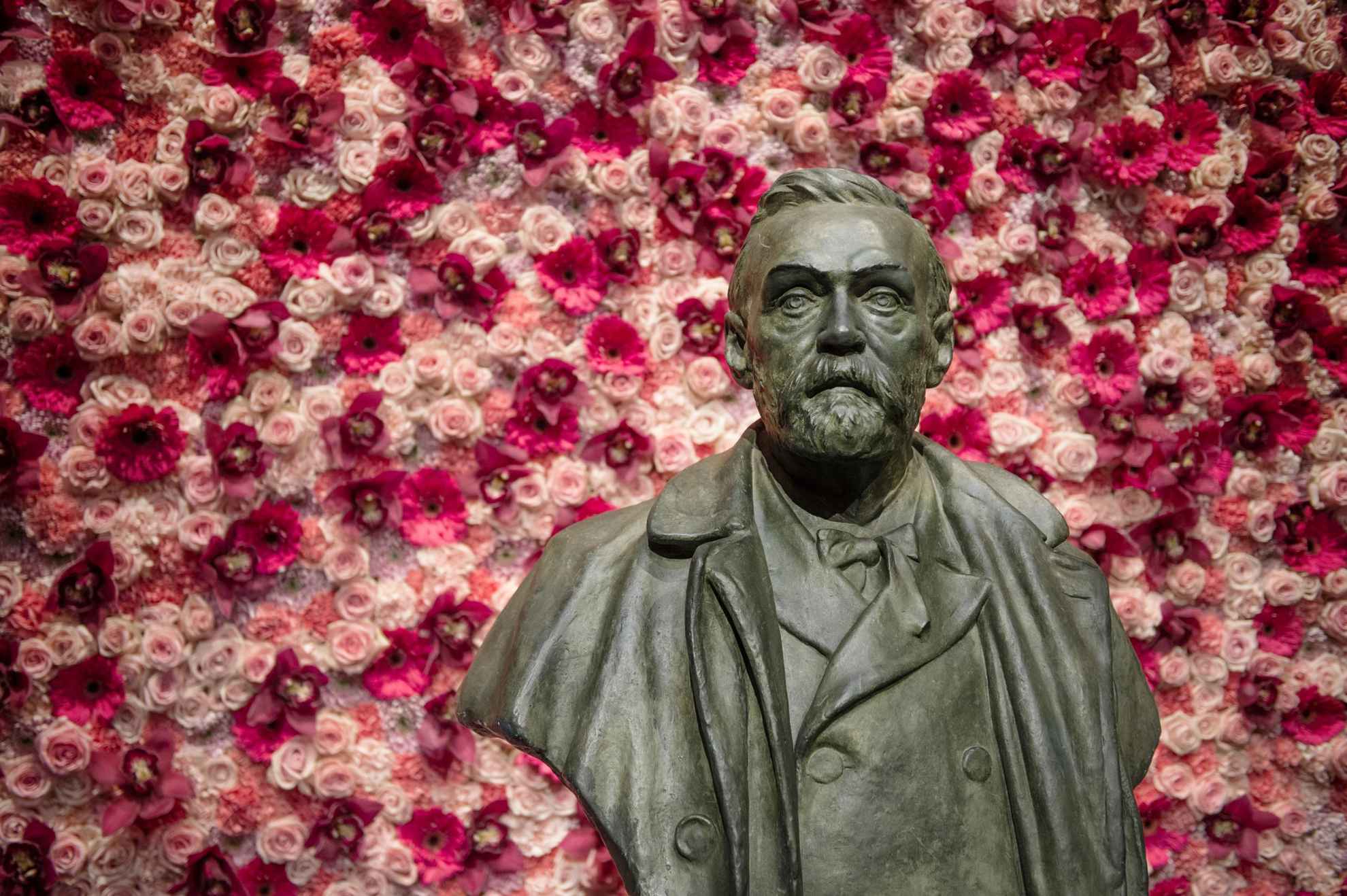 Une statue d'Alfred Nobel devant un mur décoré de fleurs roses et blanches.