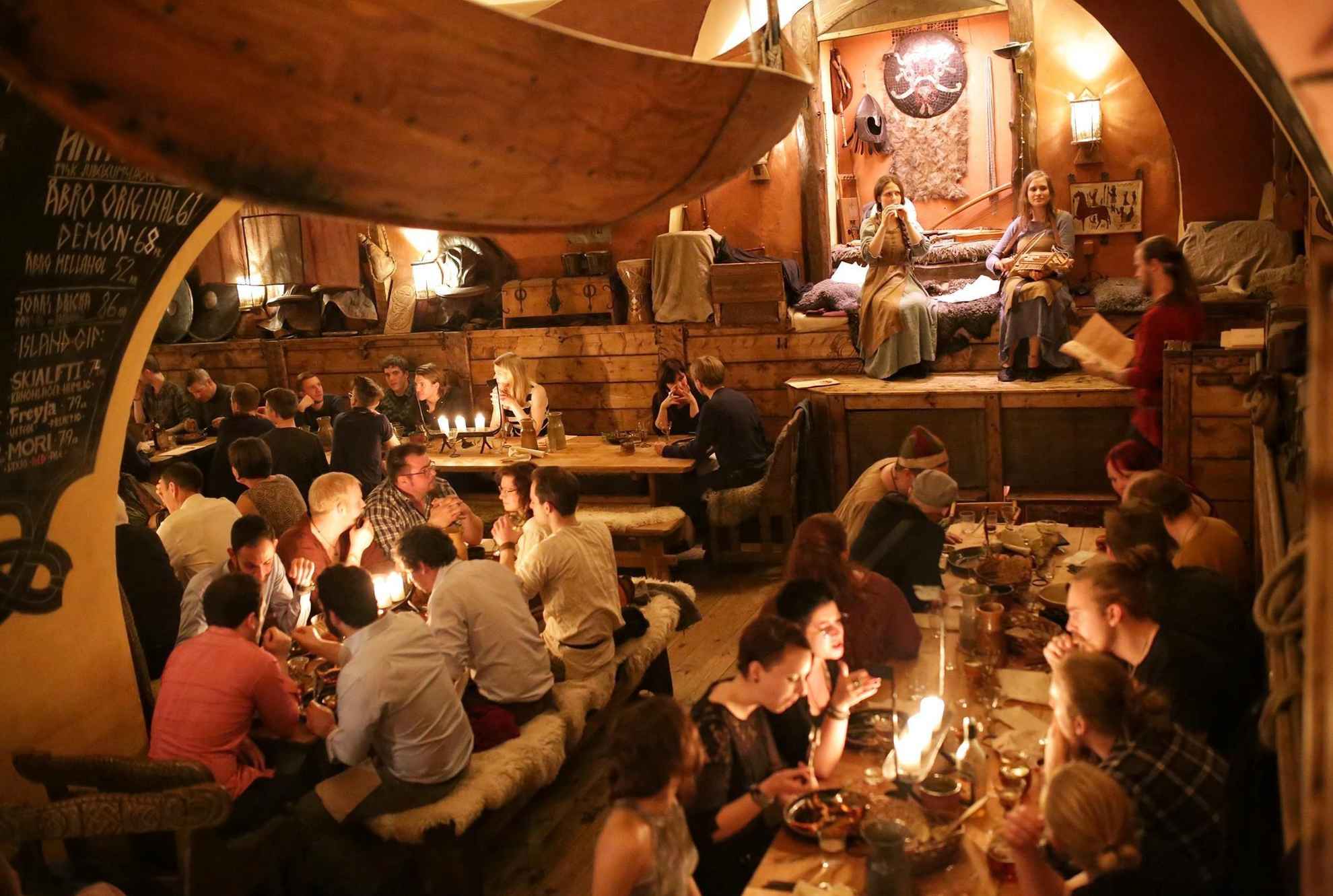 Un restaurant sur le thème des vikings rempli de monde. Sur la petite scène, deux femmes jouent de la musique.