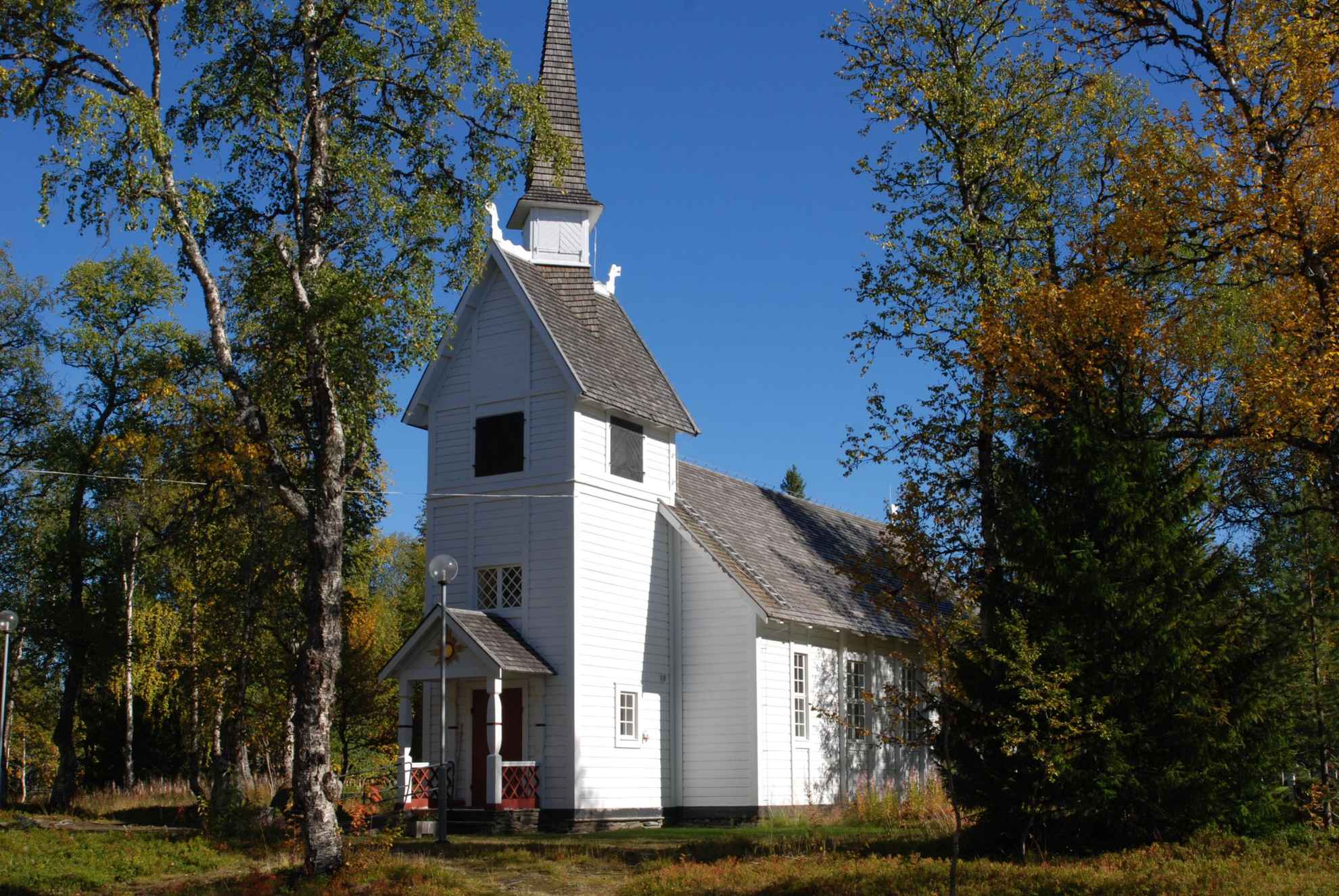Une chapelle blanche entourée d'arbres à feuilles caduques aux couleurs automnales.