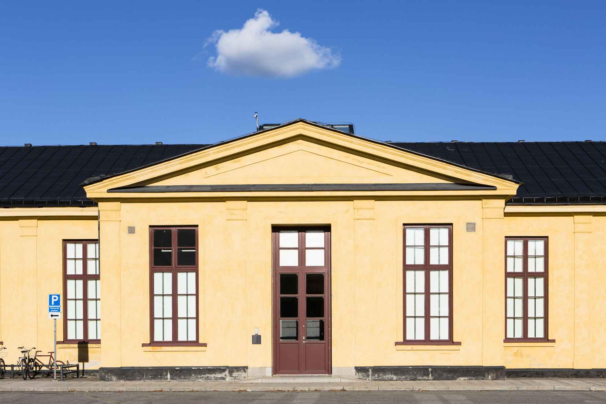 Vue sur l'extérieur d'un bâtiment jaune clair avec des fenêtres à meneaux de couleur bordeaux et une porte à double battant.