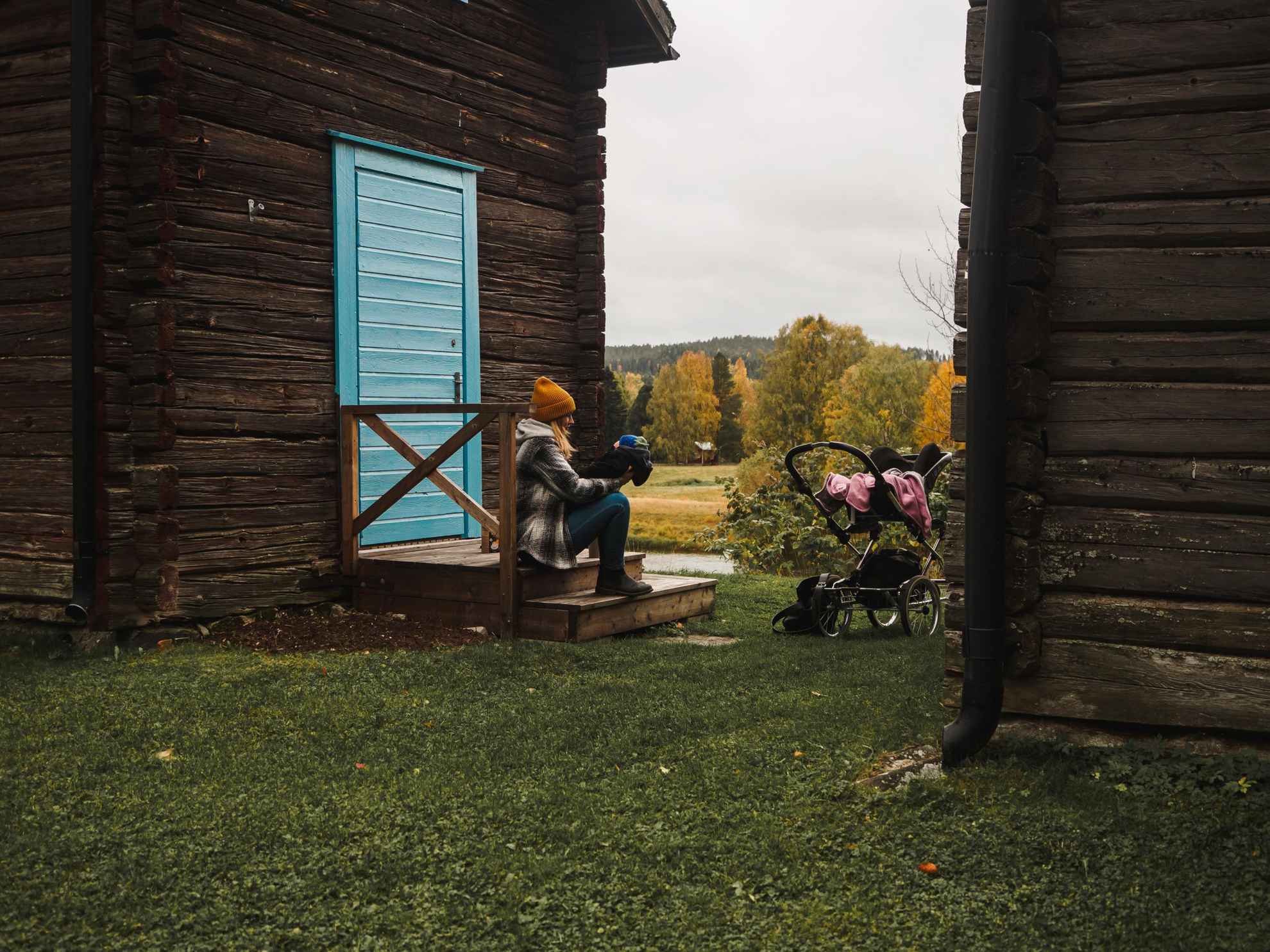 Une femme assise sur un porche en bois avec un bébé. Il y a une poussette à côté d'eux.