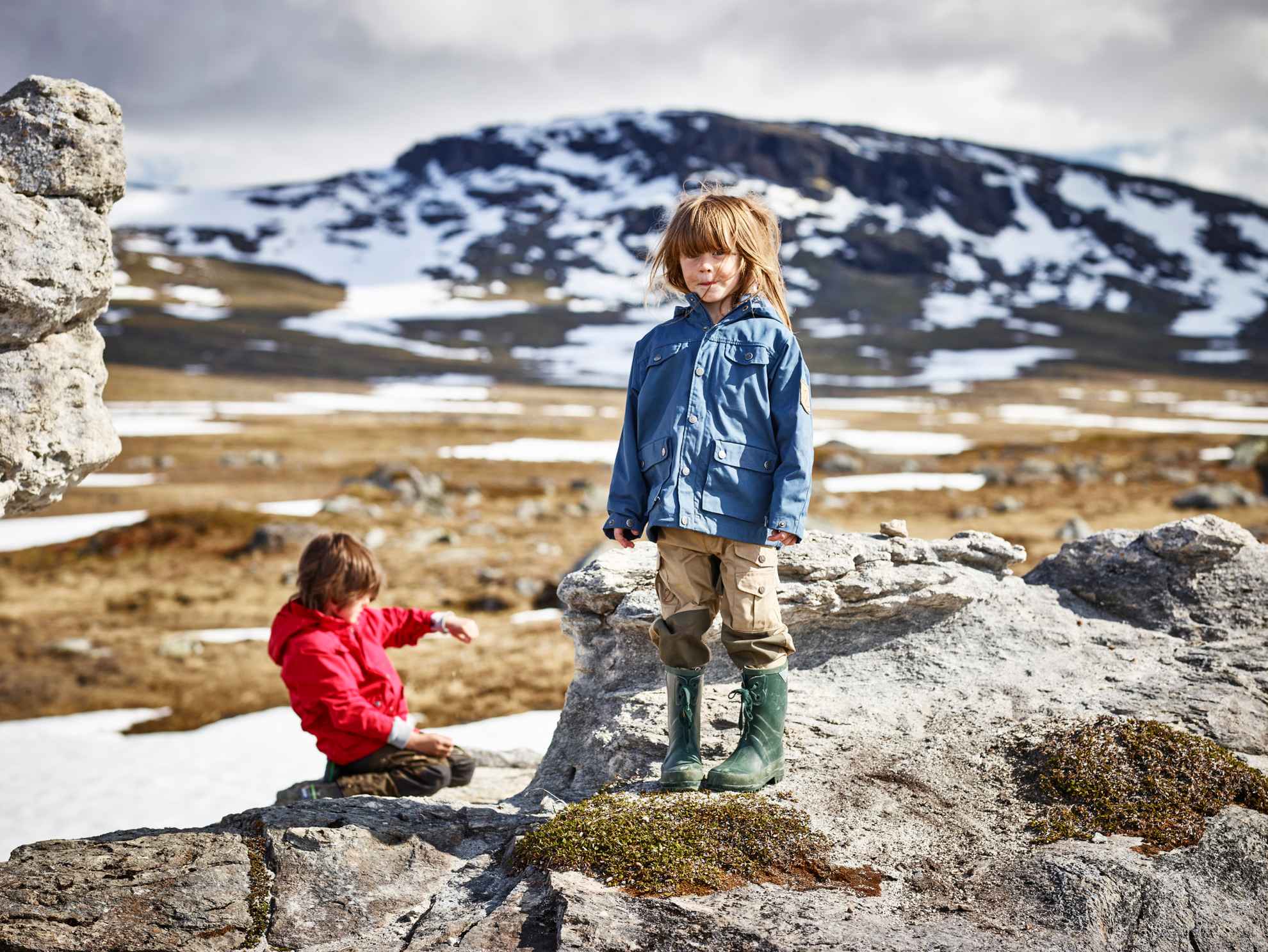 Deux enfants font une randonnée à Padjelanta, dans le nord de la Suède. Ils sont entourés d'étendues de neige et de pics montagneux.