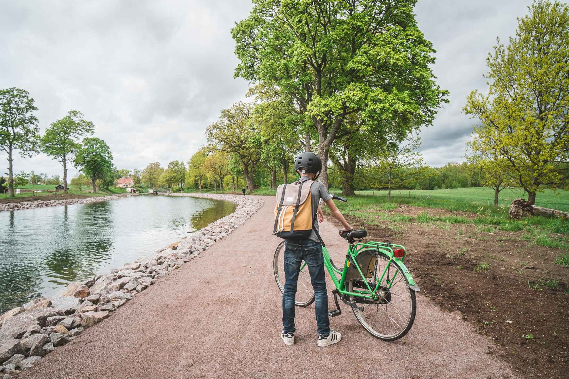 Un garçon debout à côté de son vélo vert sur une route au bord de l'eau du canal Göta.