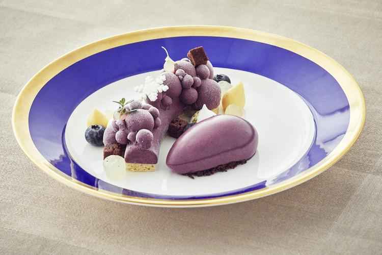 Un dessert violet avec de la garniture sur une assiette de couleurs blanc et bleu avec un bord doré.