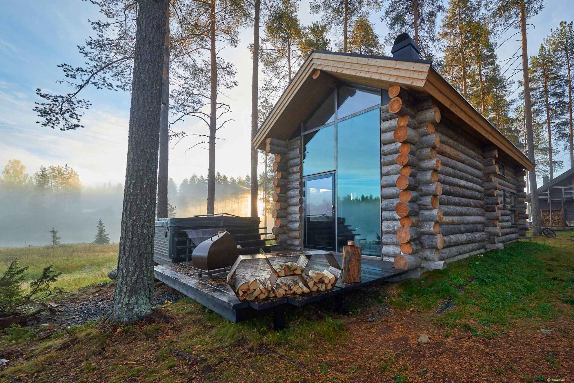 Vue d'automne sur une maison en bois avec de grandes ouvertures et un patio en bois.
