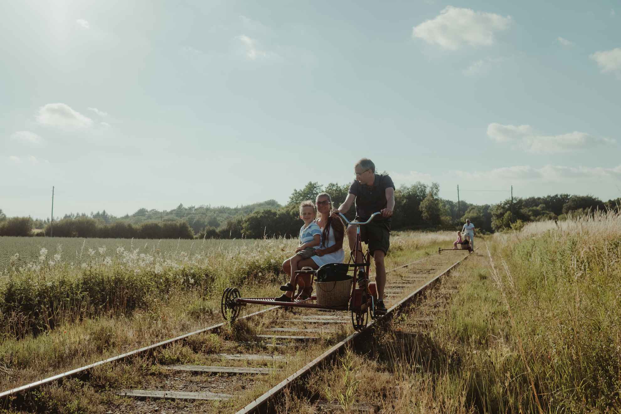 Une famille sur un vélo trolley sur une ancienne voie ferrée, entourée de champs.