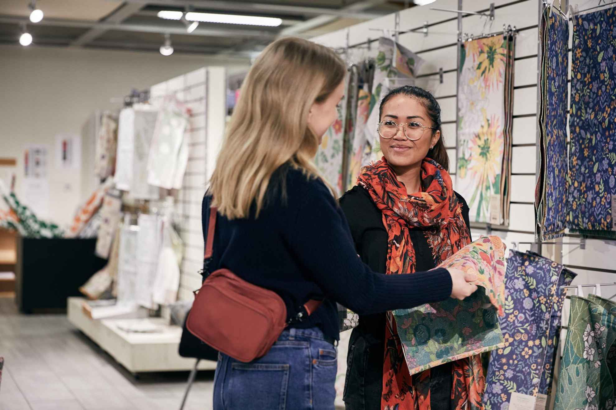 Deux jeunes femmes regardent un tissu fleuri dans une boutique de textile.