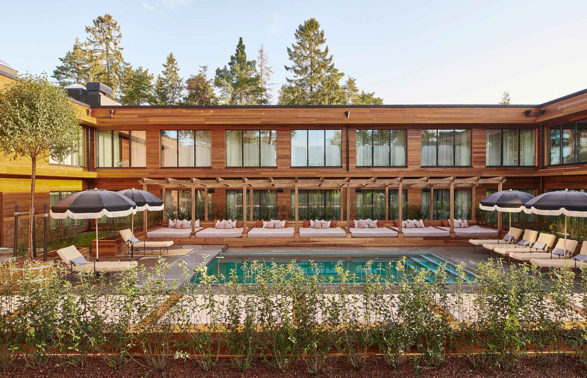 Une piscine avec des chaises longues et des parasols devant une maison en bois avec de grandes fenêtres.