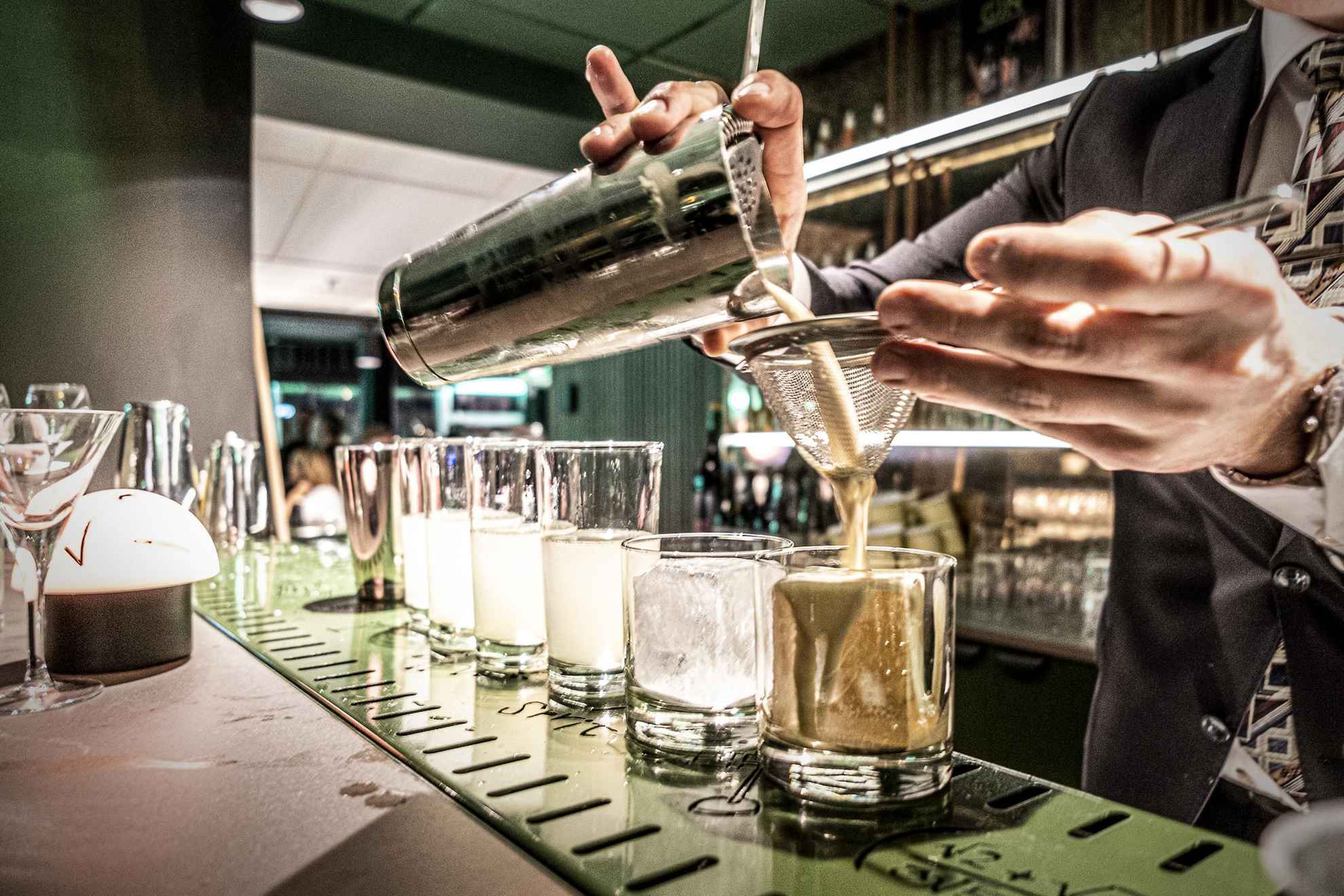 Un barman versant un cocktail dans un verre avec son shaker.