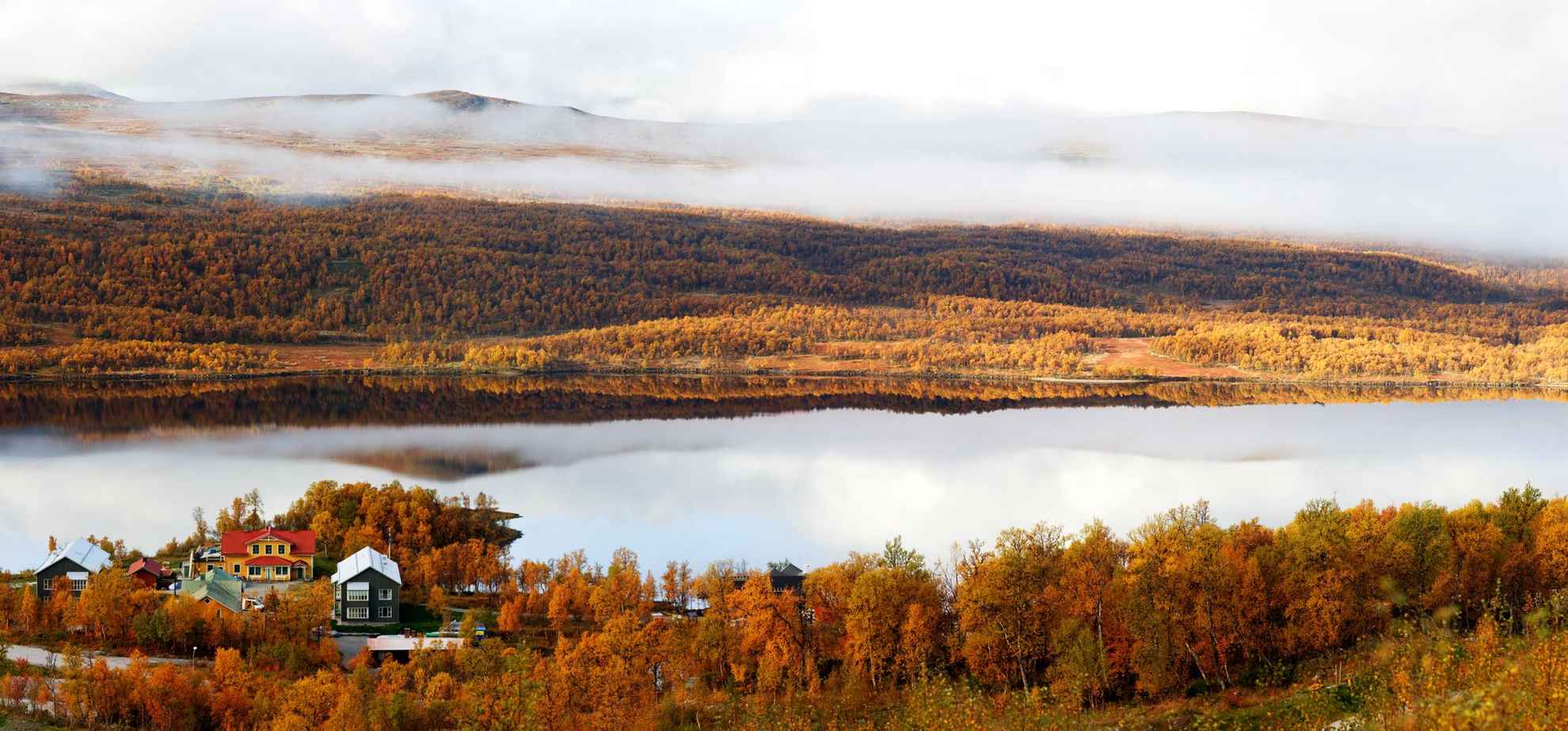 Une belle vue d'automne d'un hôtel au bord d'un lac dans les montagnes. Les arbres sont oranges et il y a du brouillard sur la montagne de l'autre côté du lac.