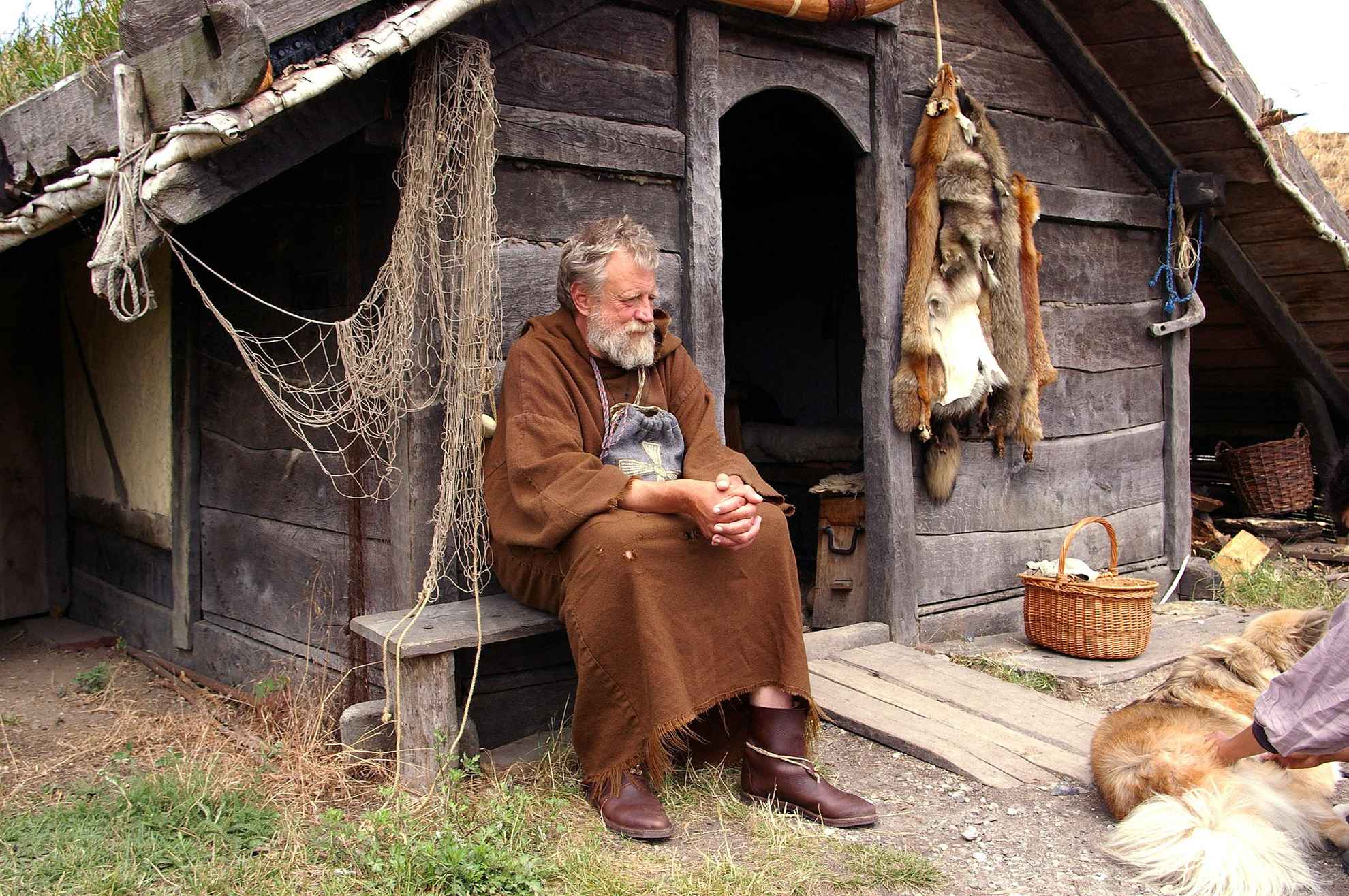 Un vieil homme habillé en viking est assis devant une vieille maison en bois.