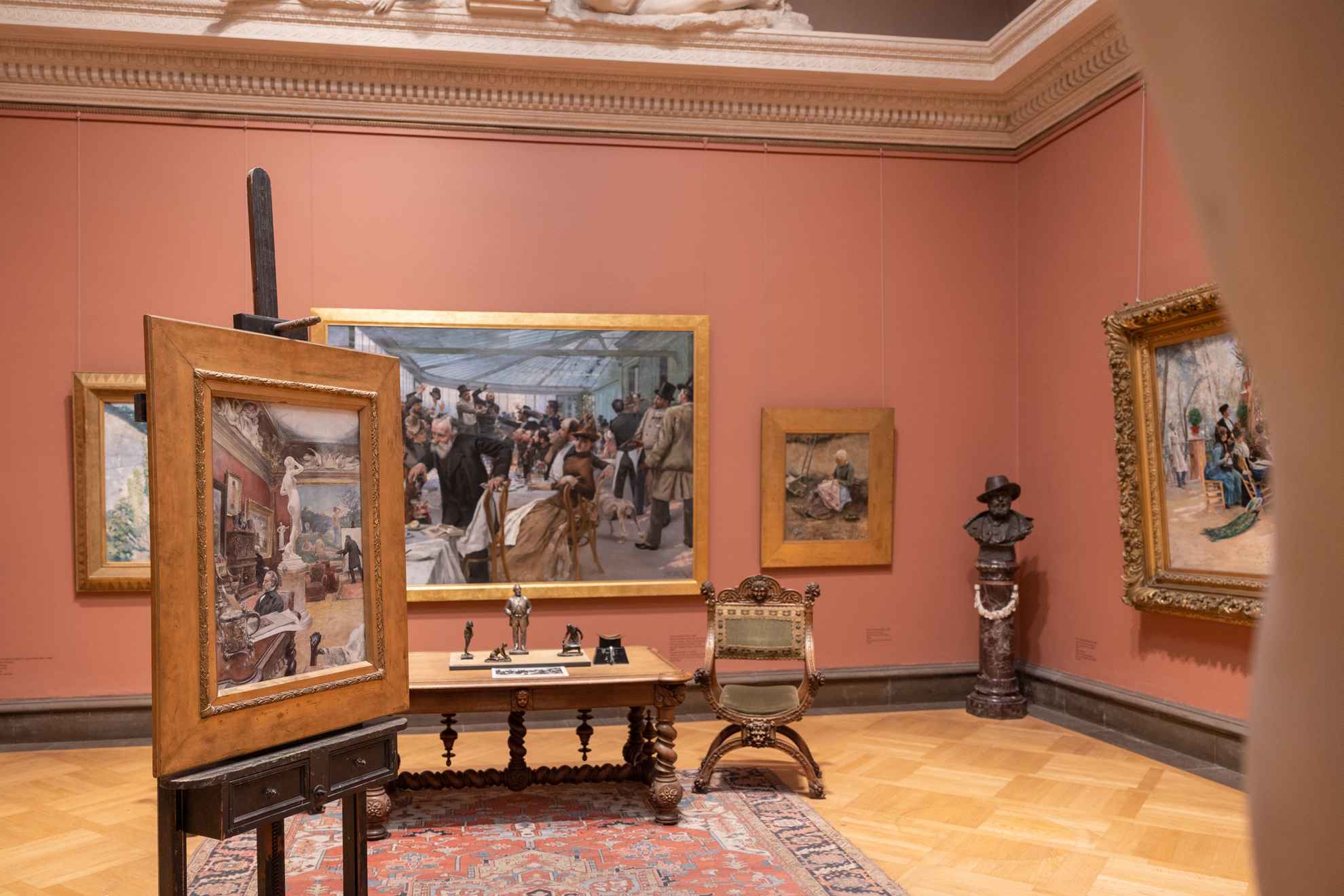 Des œuvres d'art sont exposées dans une pièce aux murs de couleur rose poudre et dont le sol en bois est recouvert d'un tapis ancien.