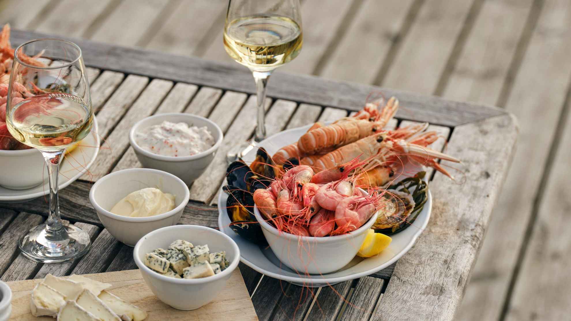 Un plateau de fruits de mer et un verre de vin blanc sont posés sur une table dressée sur un ponton.