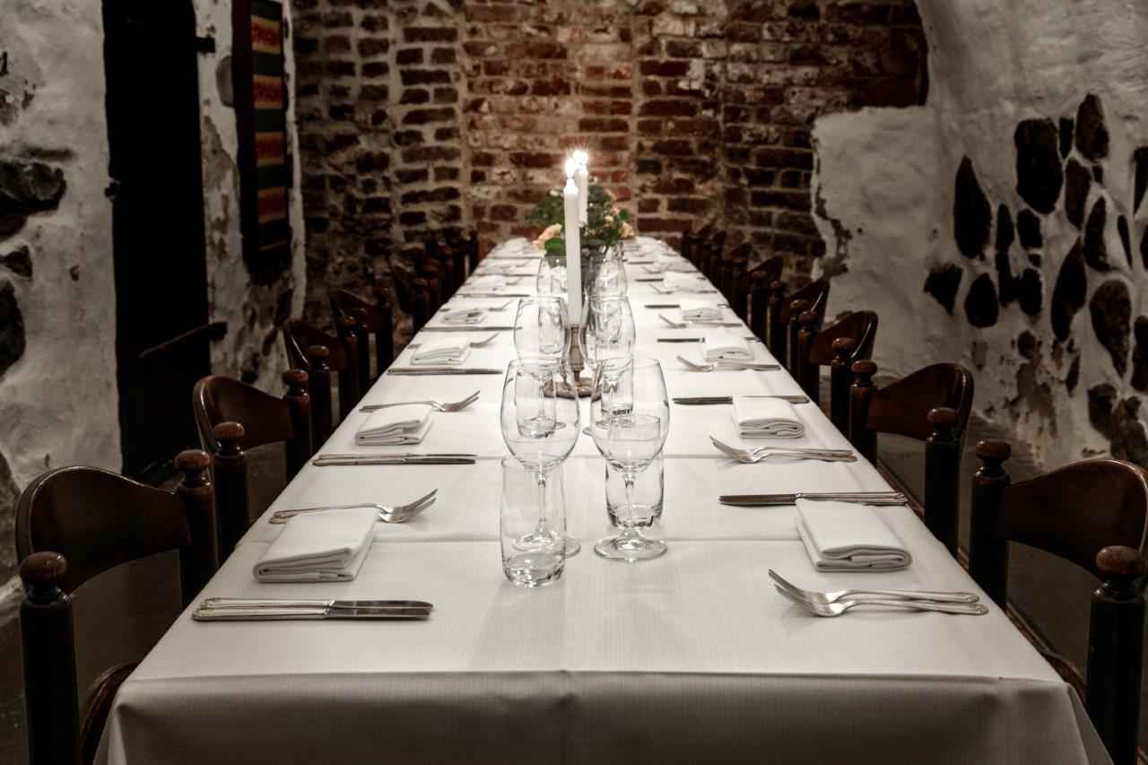Une table dressée avec une nappe blanche, des couverts, assiettes et verres.
