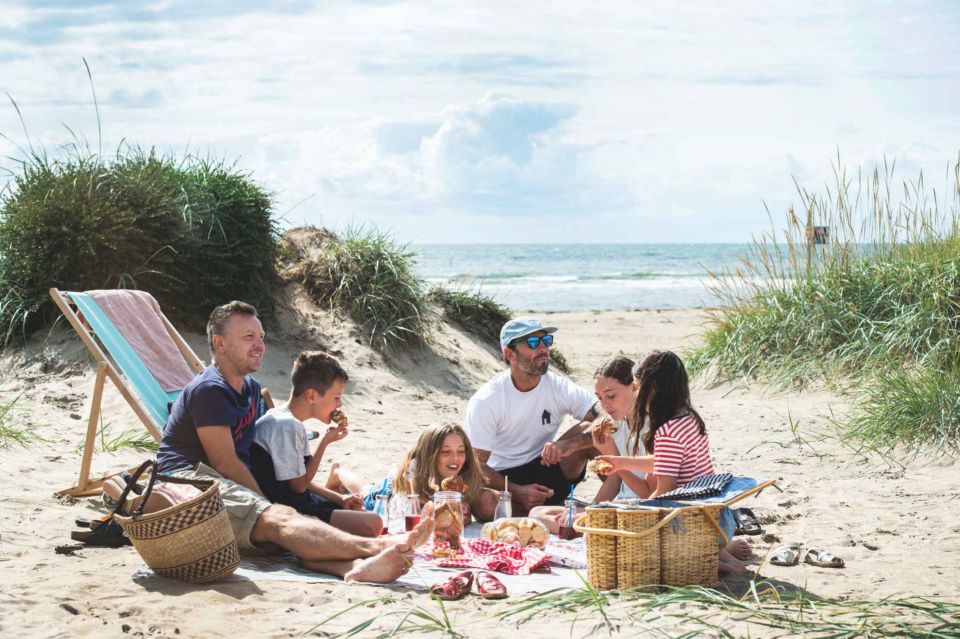 Deux hommes et quatre enfants pique-niquent sur la plage.