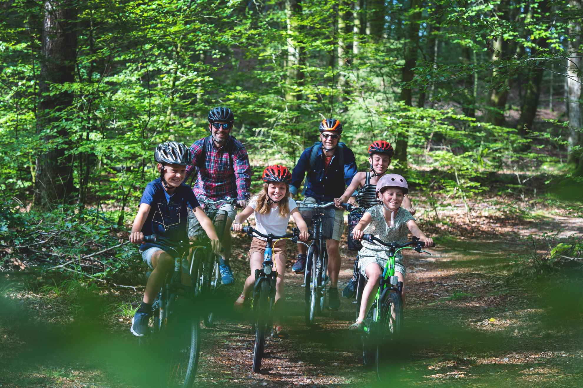 Deux hommes et quatre enfants font du vélo dans la forêt.