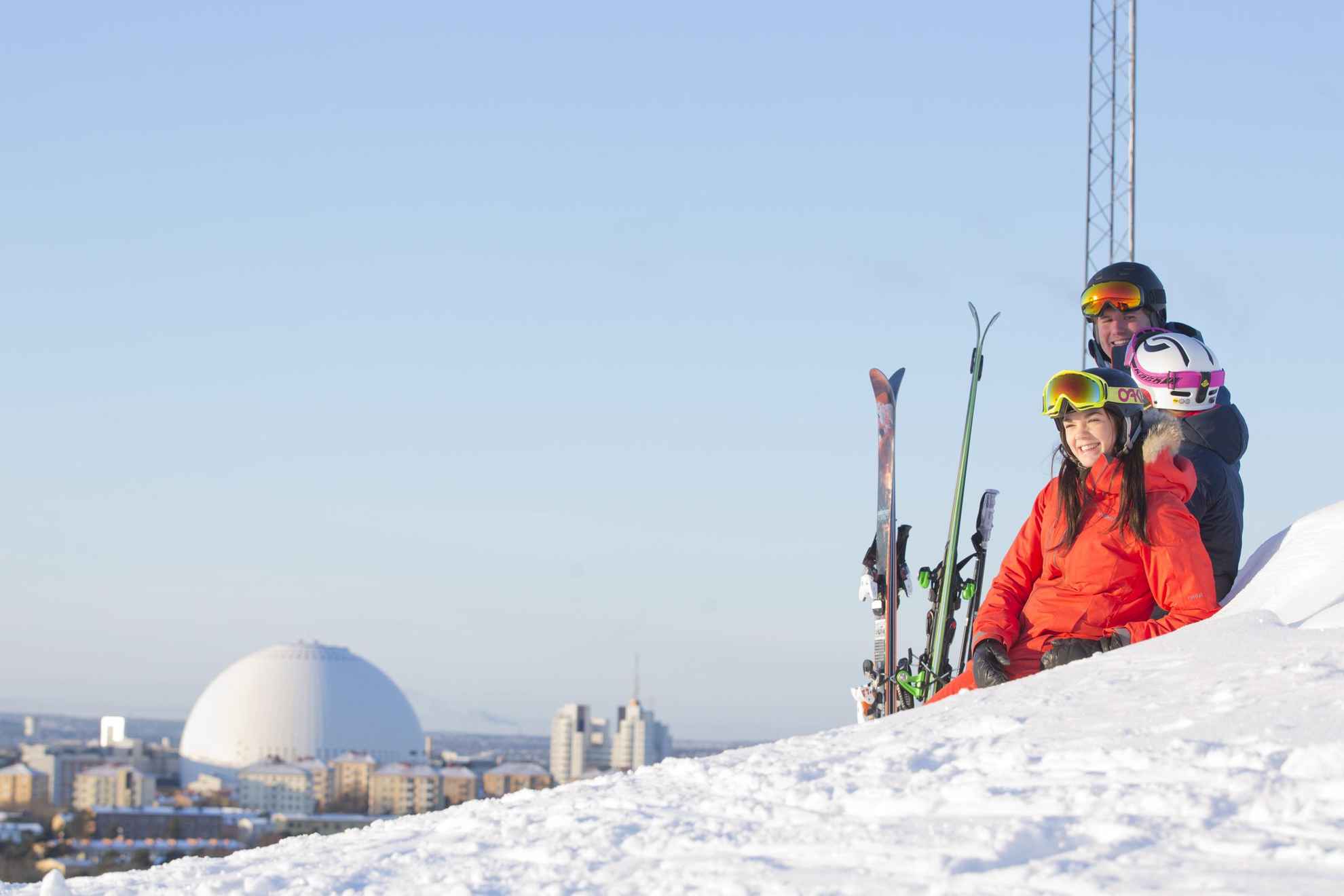 Trois personnes en tenue de ski se détendant dans la neige en profitant de la vue sur Stockholm.