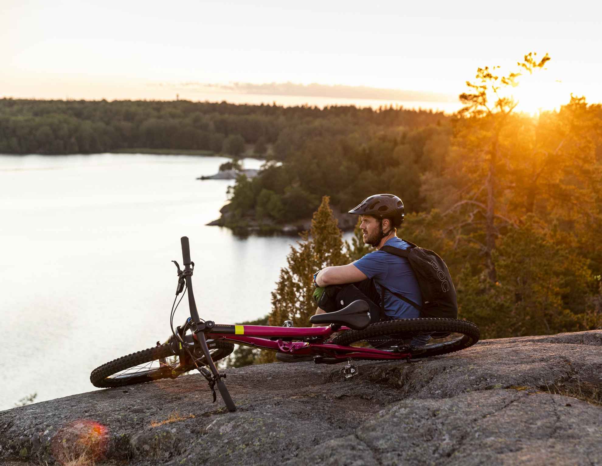 Un homme regarde la vue sur l'eau, assis depuis un rocher avec un vélo à côté de lui.