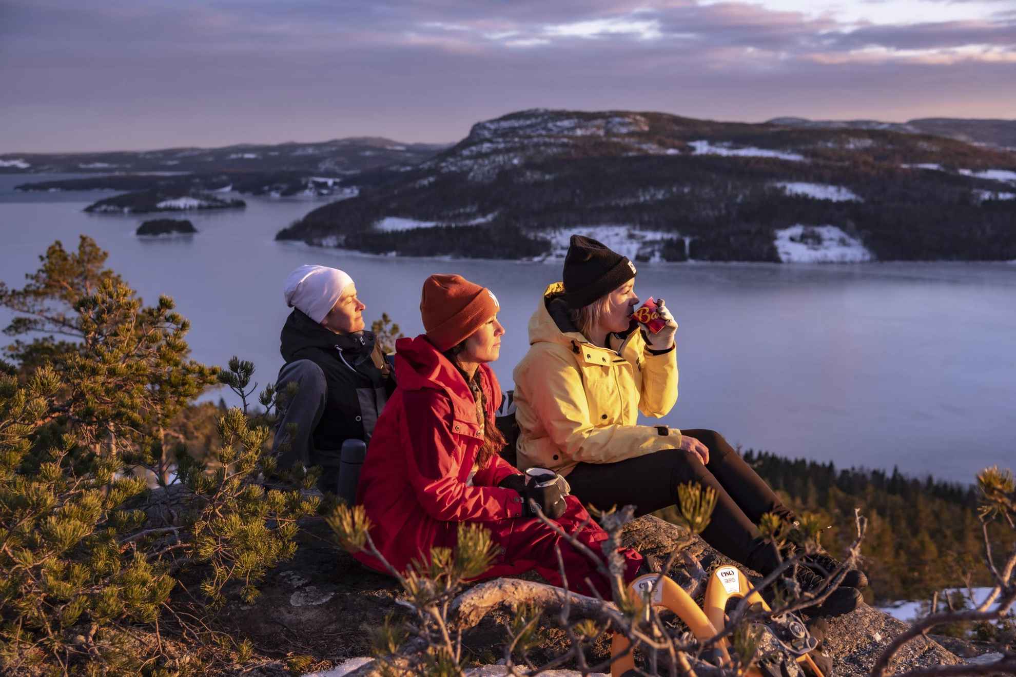 Trois personnes admirent le soleil tout en buvant une tasse de café en haut d'une colline en hiver.