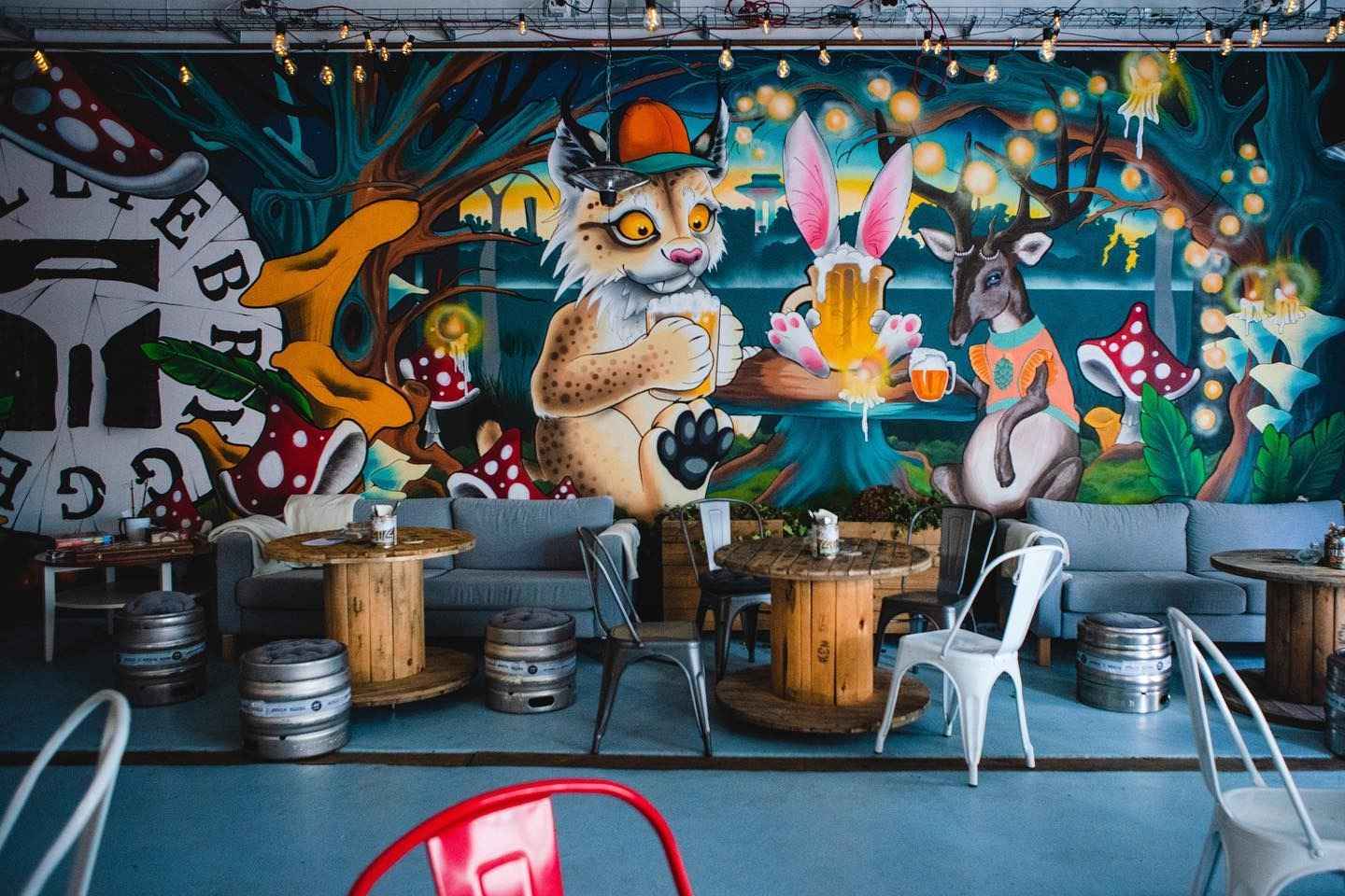 Table en bois avec des tonneaux de bière en guise de chaises, avec un mur coloré en graphite derrière.