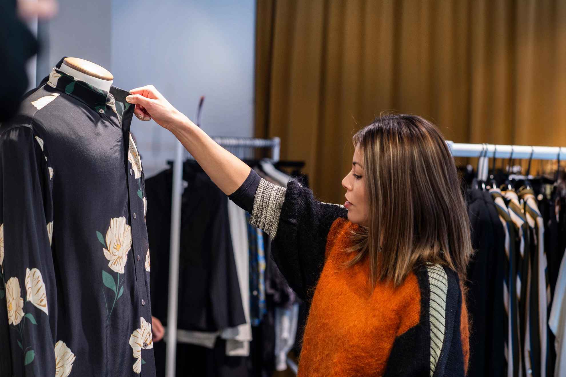 Une femme touche et regarde une chemise à motif floral sur un mannequin dans un magasin.