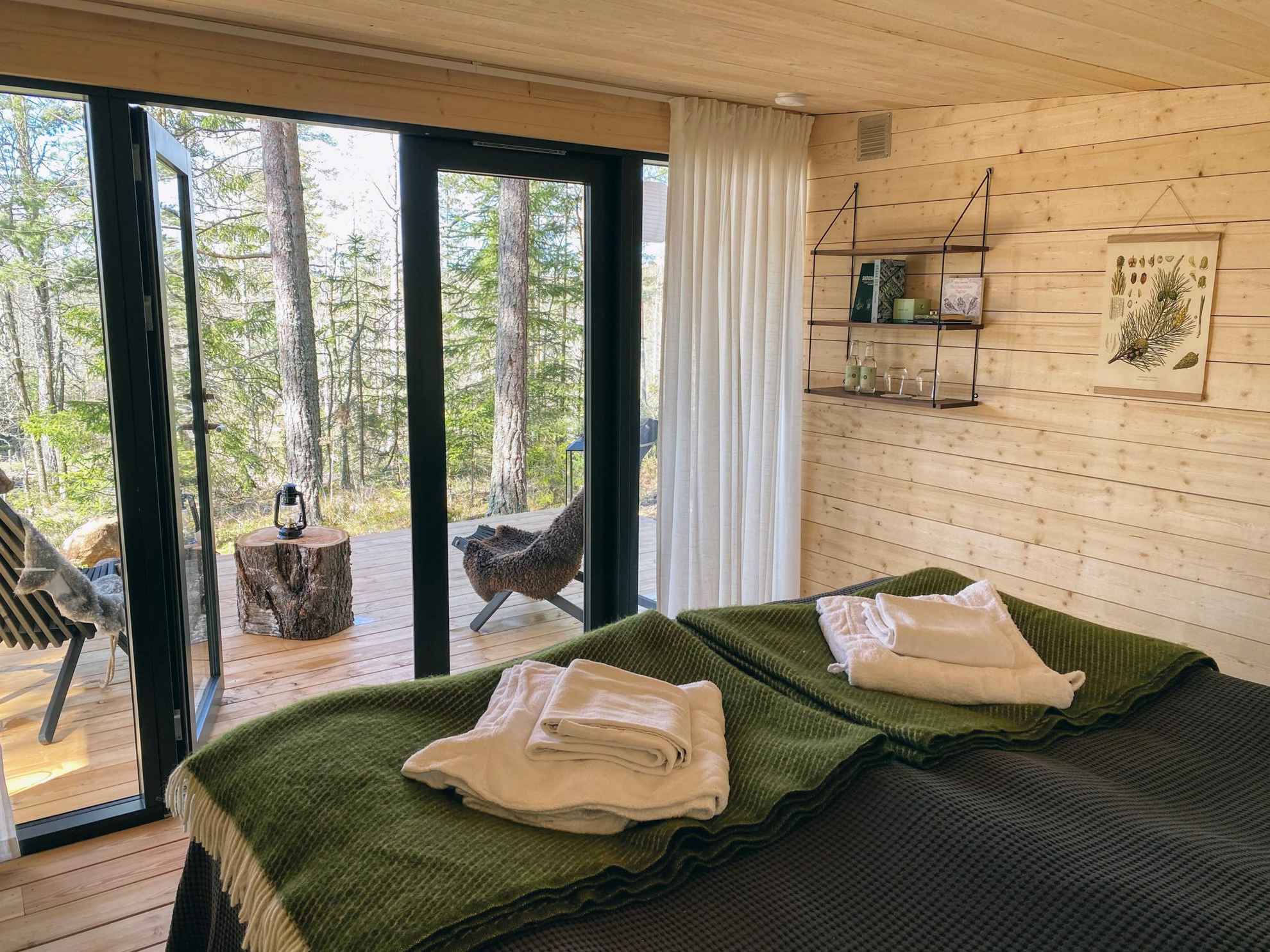 Deux lits se trouvent dans une pièce avec les murs et le sol en bois. La chambre a des portes vitrées donnant sur la nature et sur un patio disposant de deux chaises.