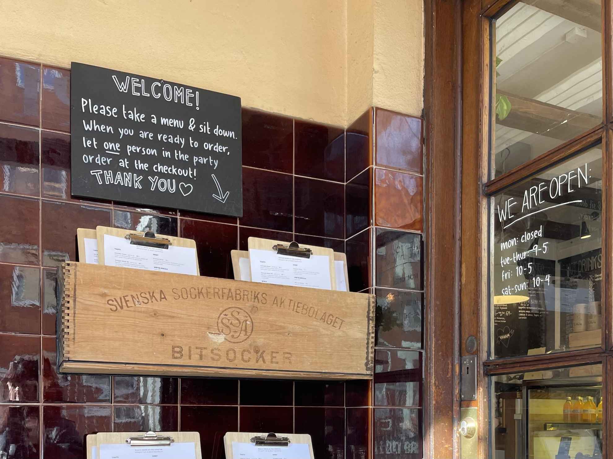 Un mur avec une petite pancarte de bienvenue et des menus rangés dans une caisse.