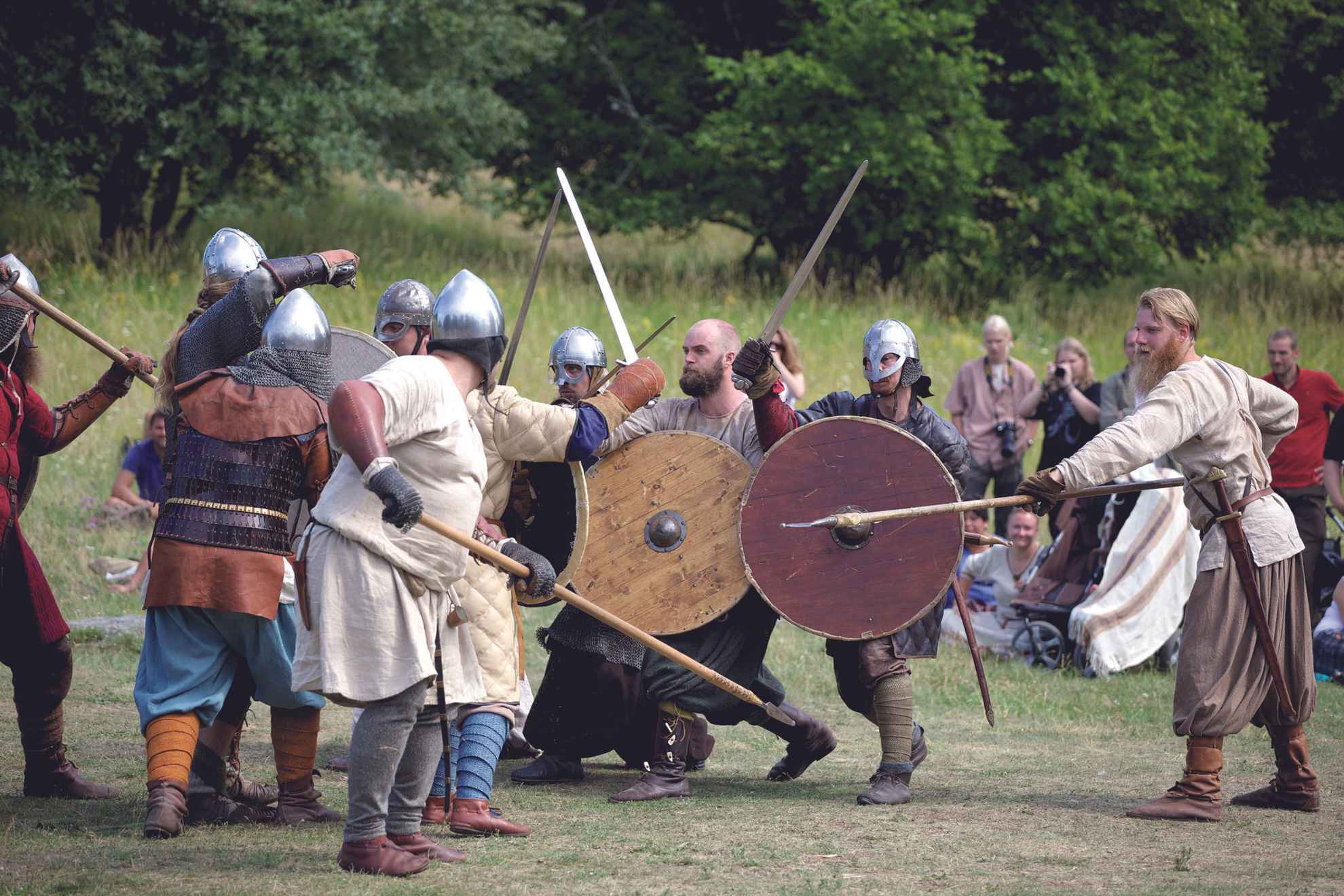 Un groupe de personnes, habillées avec des vêtements vikings, reconstitue une bataille avec des lances, des épées et des boucliers.