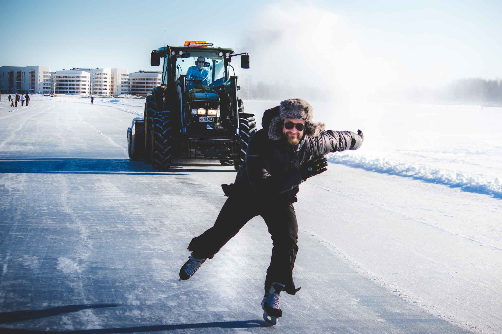 Une personne vêtue de noir patine sur la glace avec un tracteur derrière elle.