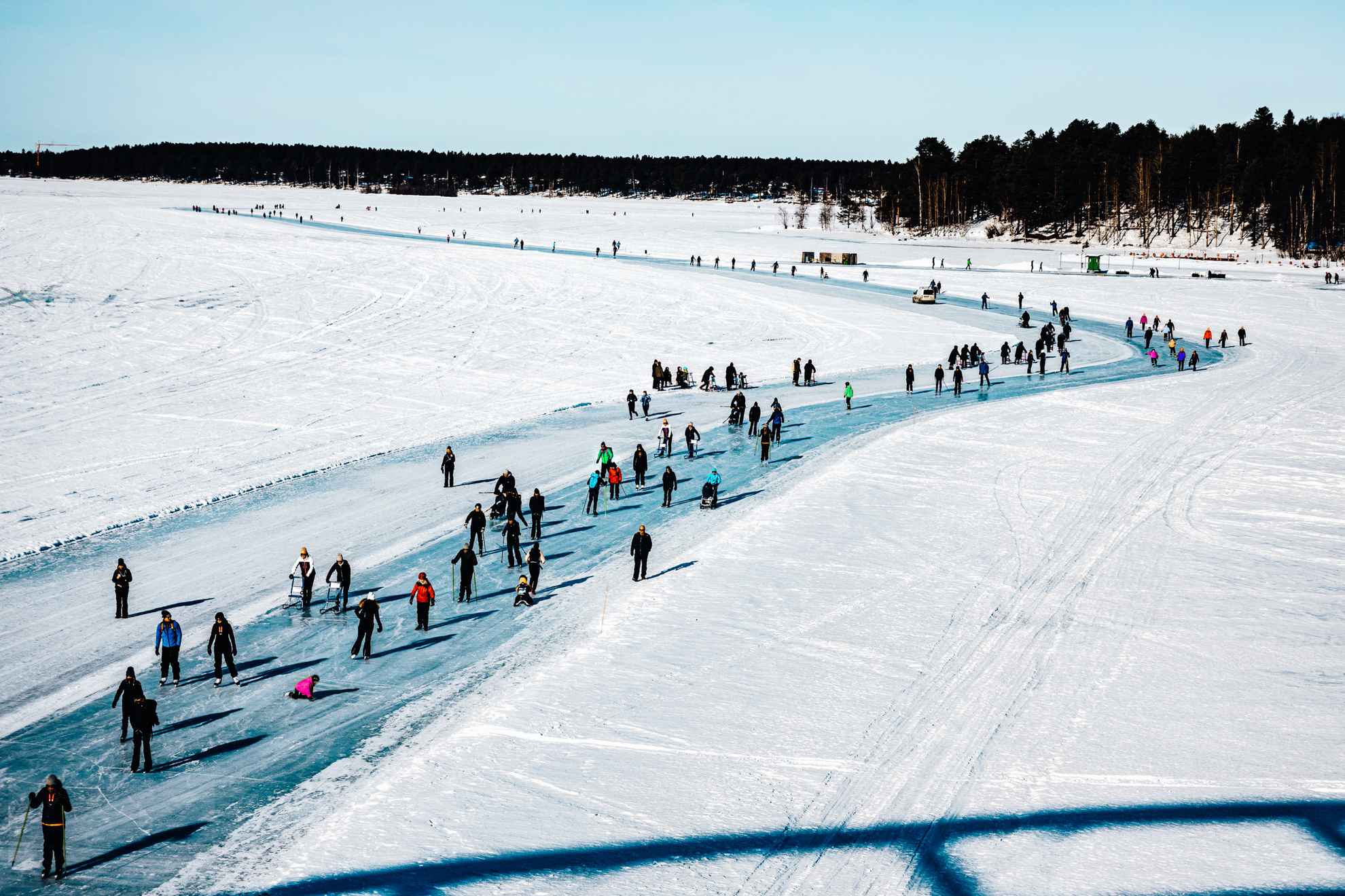 Des gens marchent et patinent sur la piste de glace ensoleillée qui entoure Luleå.