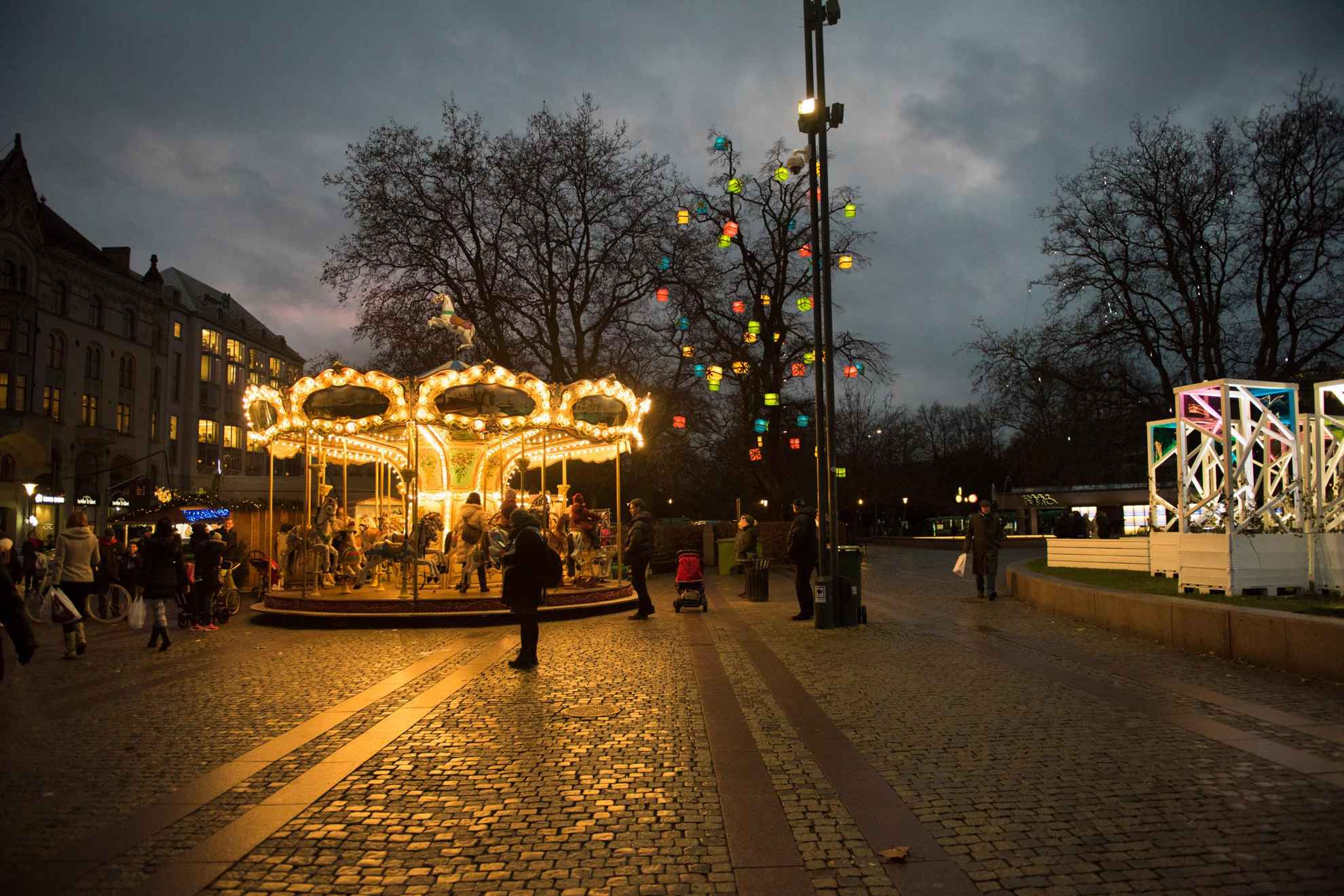 À la nuit tombée, une place publique avec des lumières colorées et un carrousel.