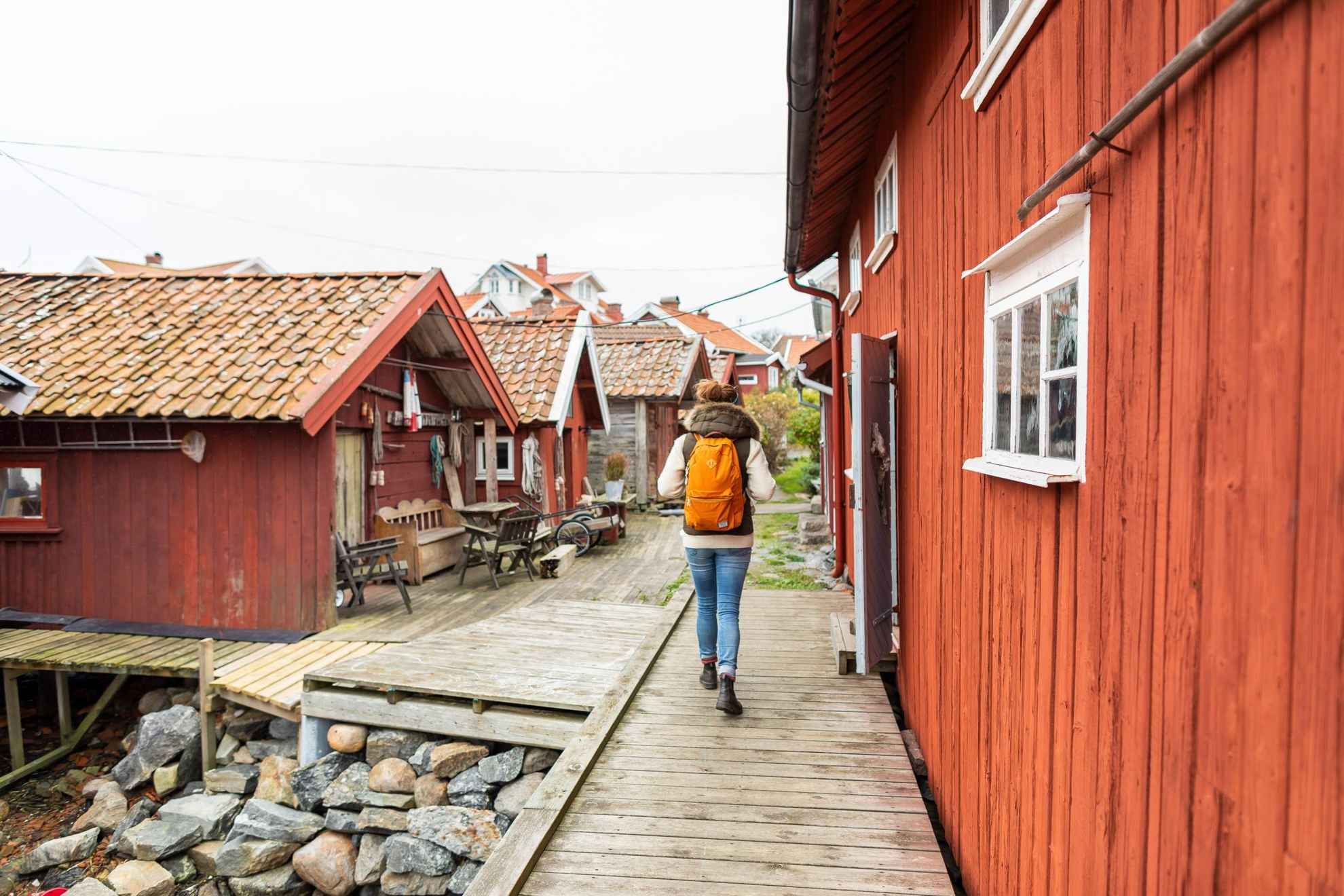 Une personne avec un sac à dos se promène parmi des maisons en bois rouges.