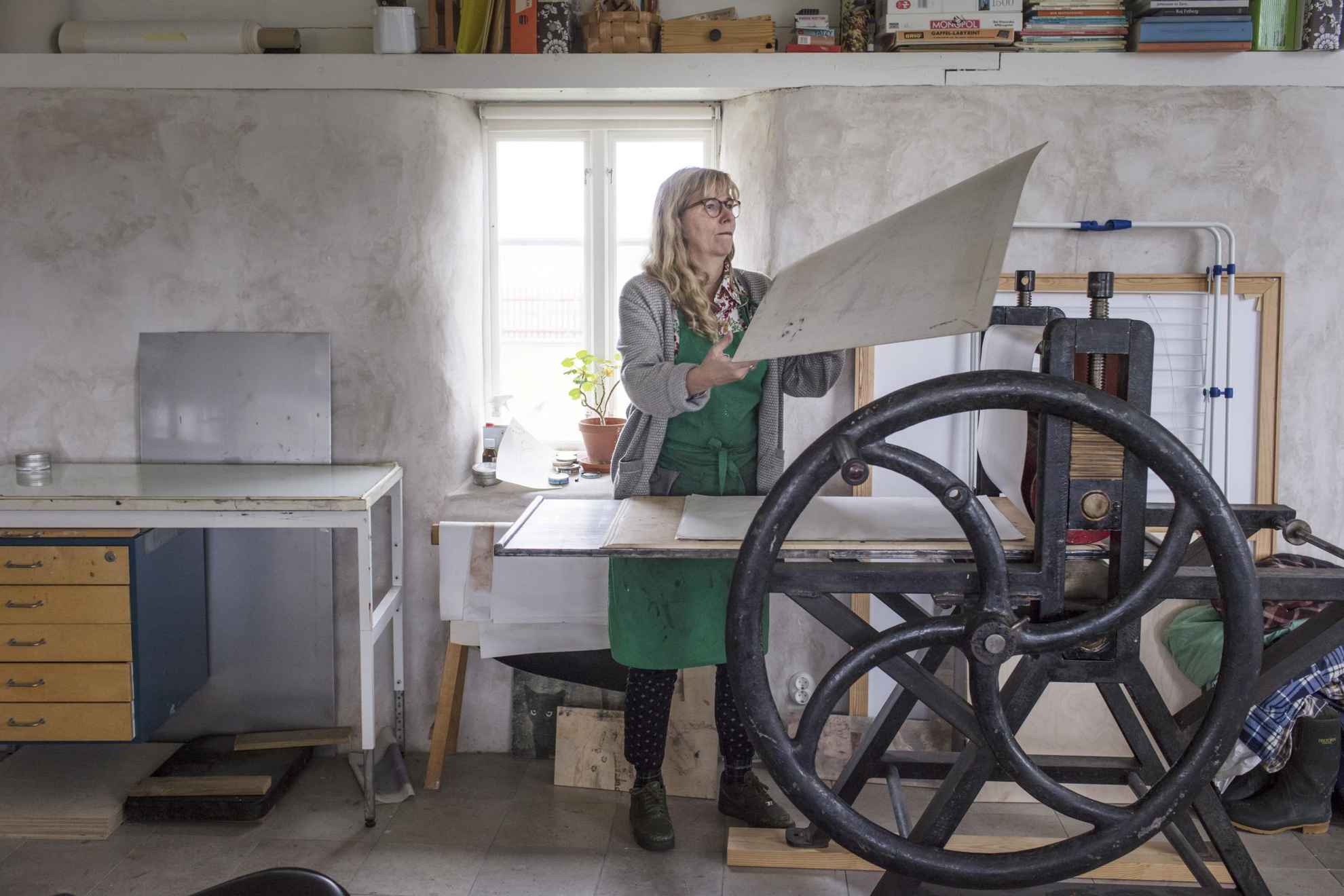 The artist Karin Mamma Andersson is working next to a large iron hand press in her studio.