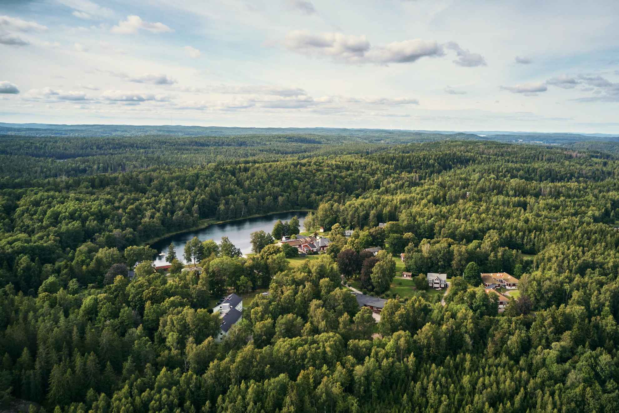 Vue aérienne de la forêt Kroppefjäll en été. On voit plusieurs maisons en bois disséminées entre les arbres de la forêt.