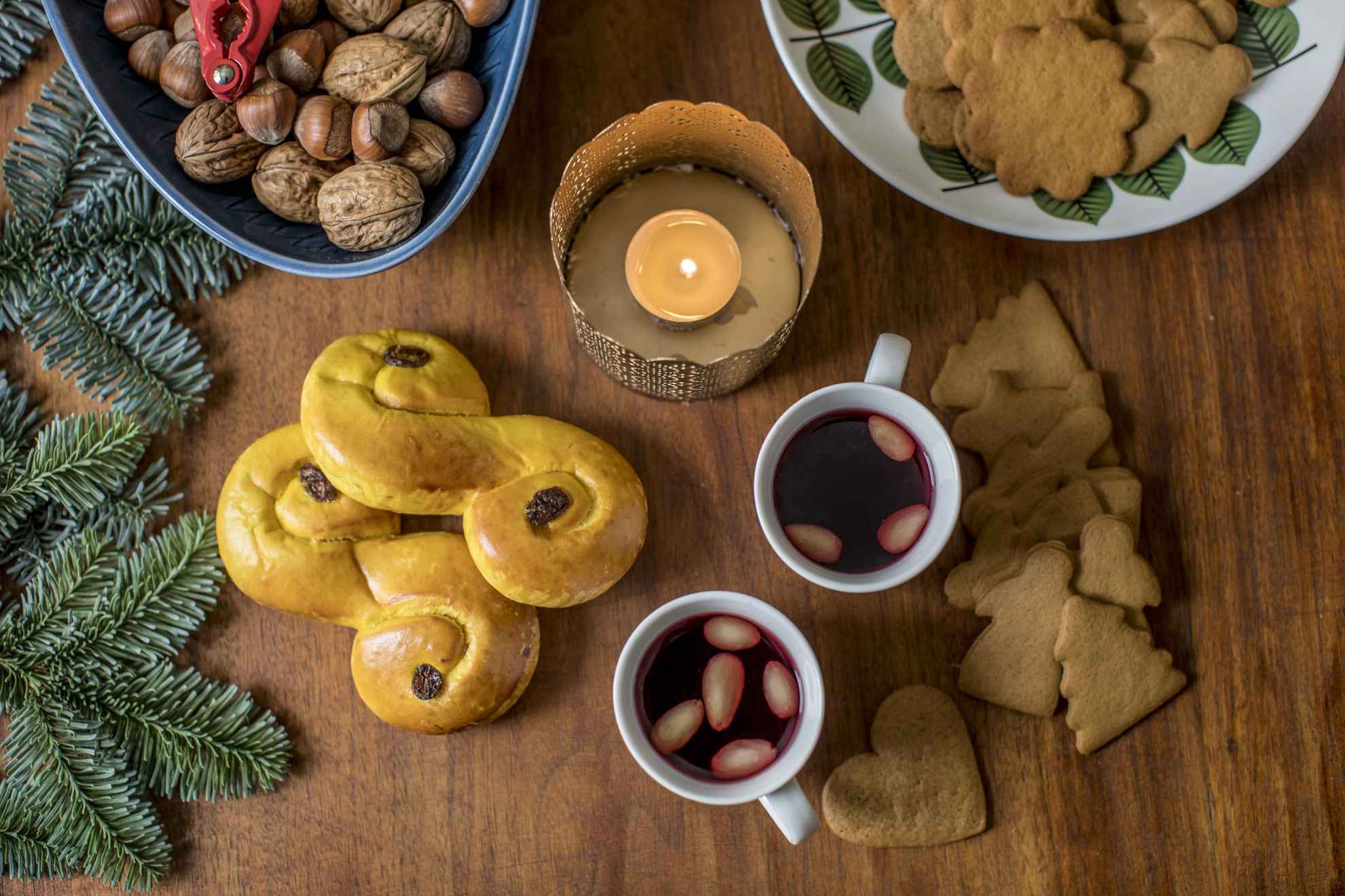 Une table garnie de délices et de décorations de Noël typiquement suédois, de vin chaud, de noix, de biscuits au gingembre, de lussebullar et de branches de sapin.