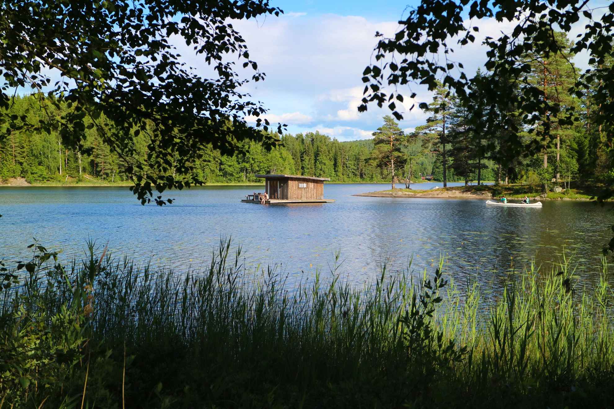 Une cabane flottante de Naturbyn sur un lac. Une personne passe à côté en canoë. Le lac est entouré d'arbres.