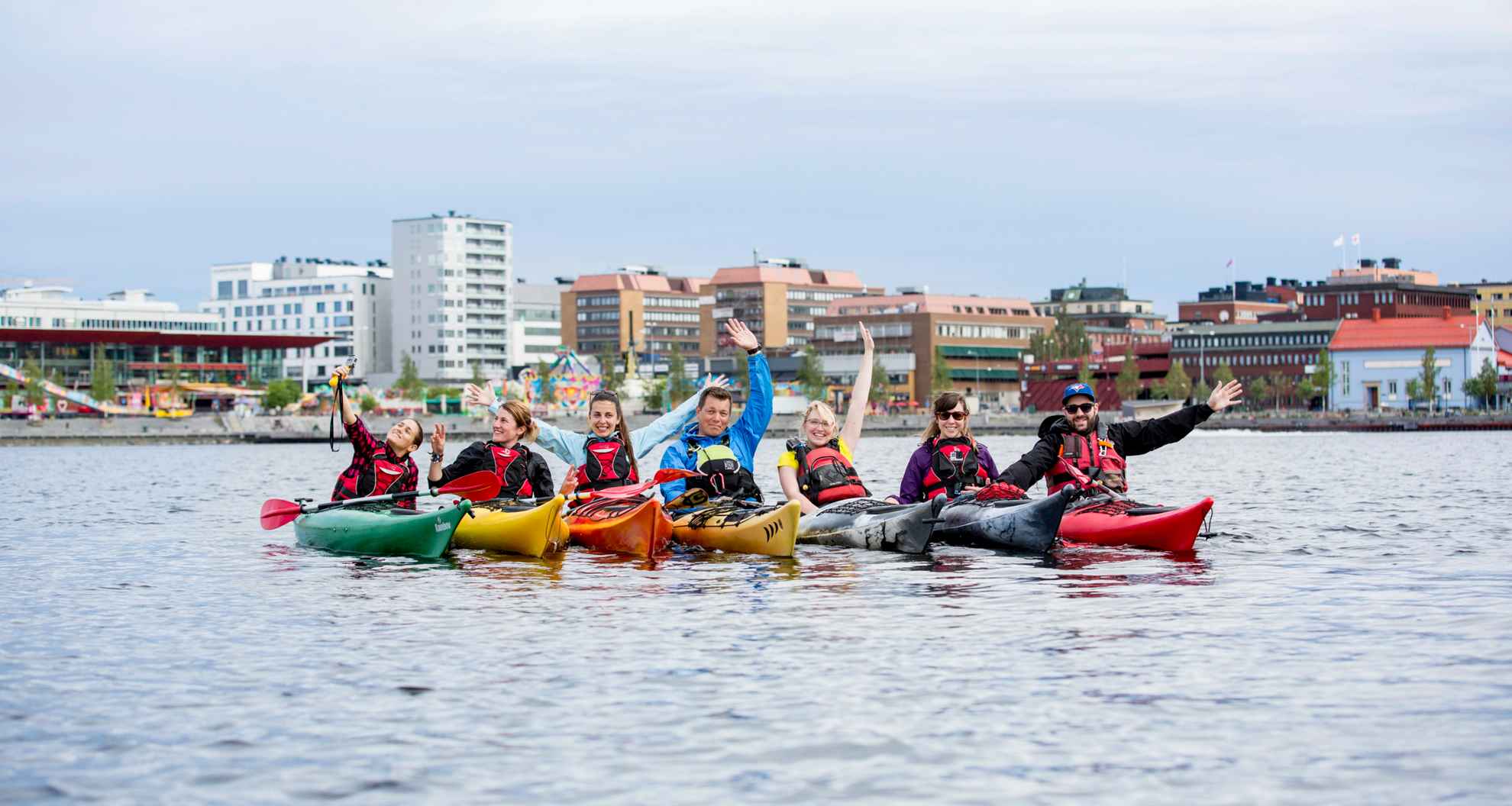 Un groupe de sept personnes en train de faire du kayak. Elles sont rassemblées et font face à la caméra dans la mer en face de la ville de Luleå.