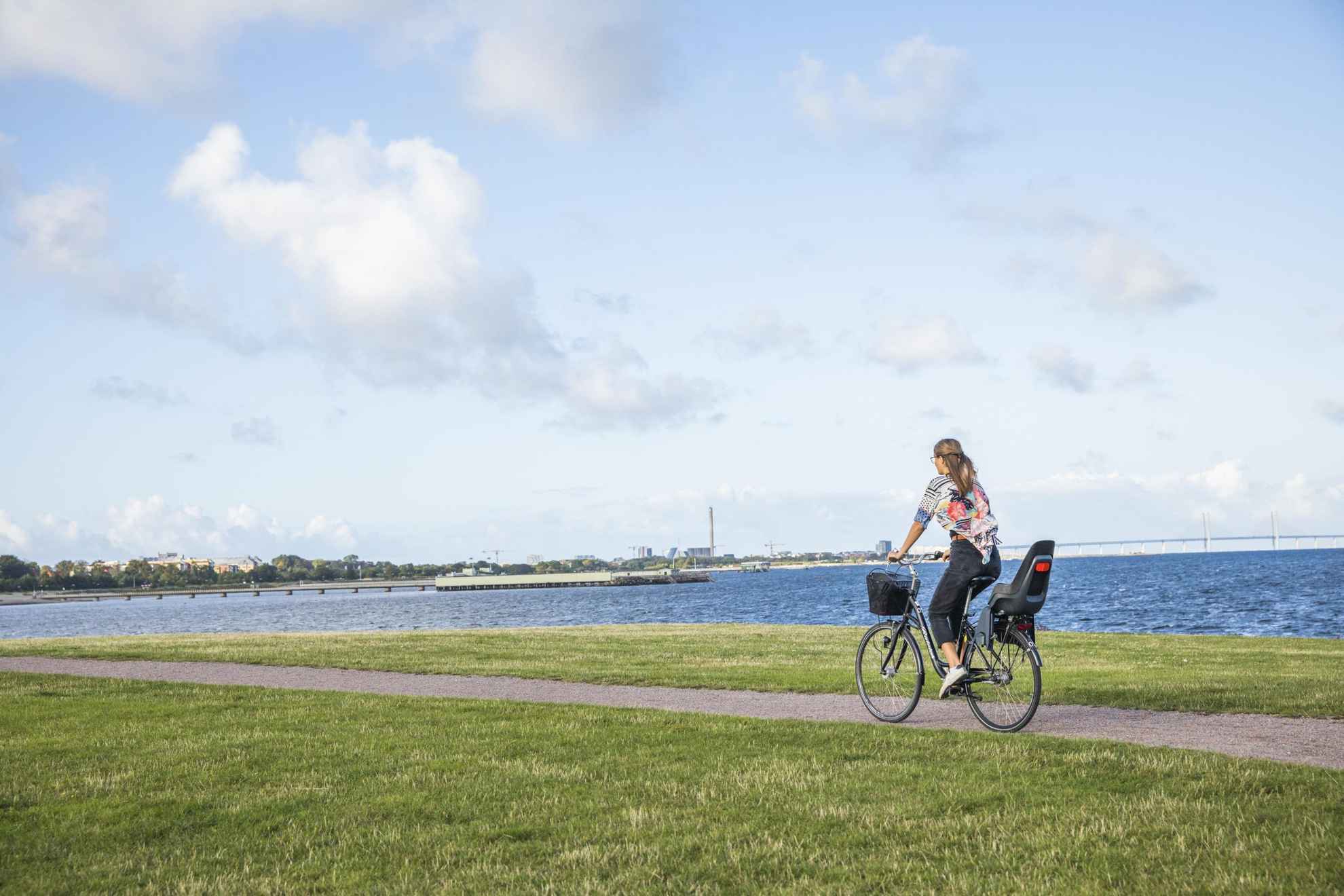 Une femme fait du vélo sur un chemin goudronné le long du rivage dans le quartier de Västra Hamnen à Malmö.