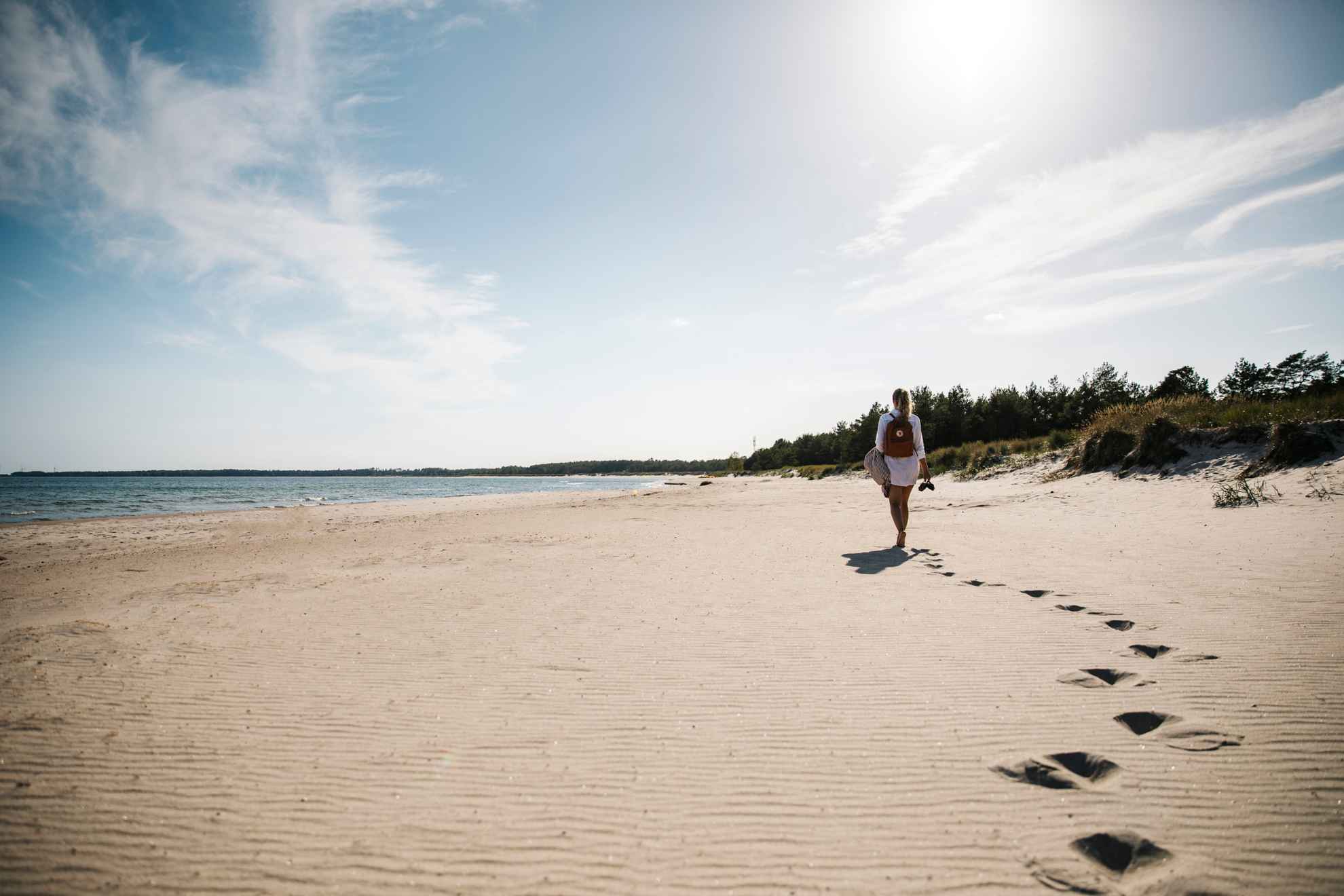 Une femme marchant sur une plage de l'île d'Öland, sac à dos et chaussures à la main.