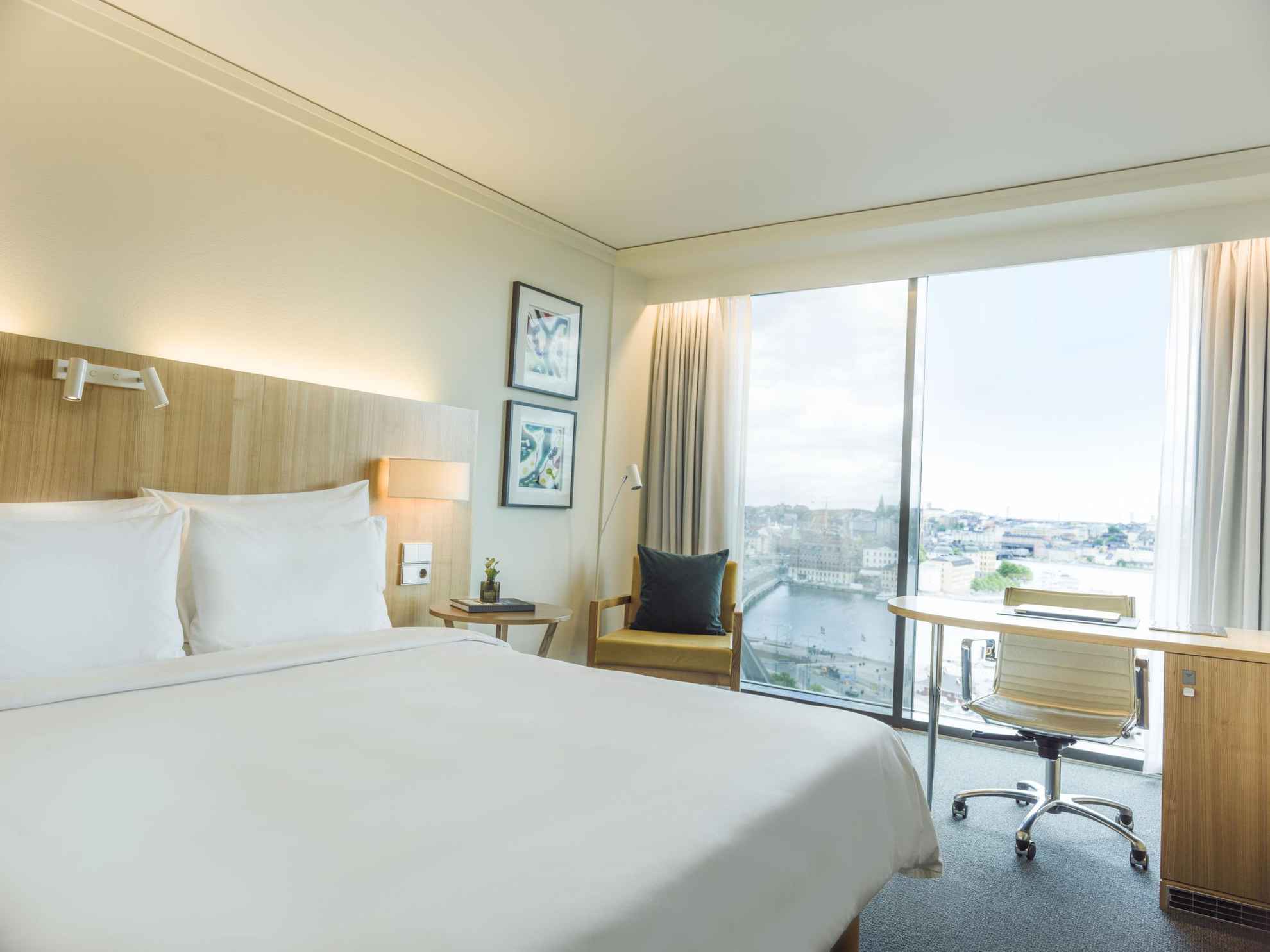 Une chambre d'hôtel avec un lit double et des draps blancs. Il y a de grandes fenêtres donnant sur l'eau.