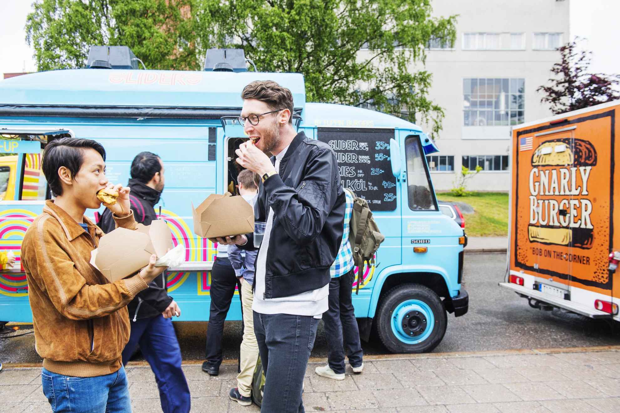 Des personnes mangent avec les mains de la nourriture dans de petites boîtes en carton à côté d'un food truck à Stockholm.