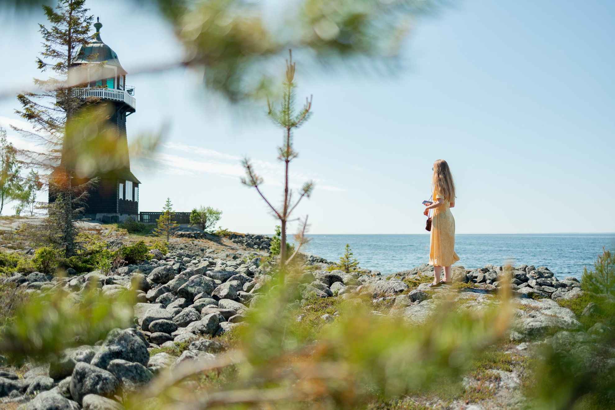 Une femme se tient debout sur une rive et regarde devant elle en direction d'un phare.