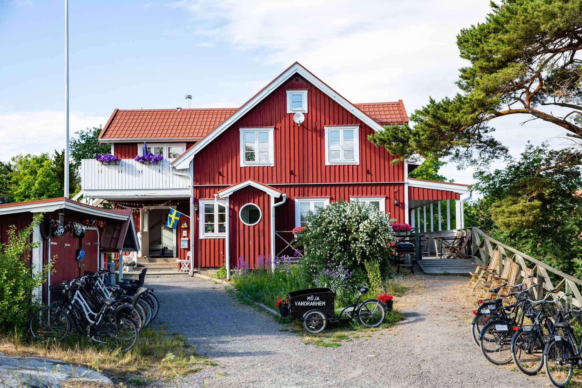Une maison en bois rouge avec des bordures blanches en été. Il y a plusieurs vélos à l'extérieur de la maison. Sur l'un des vélos, il est écrit "Möja Vandrarhem".